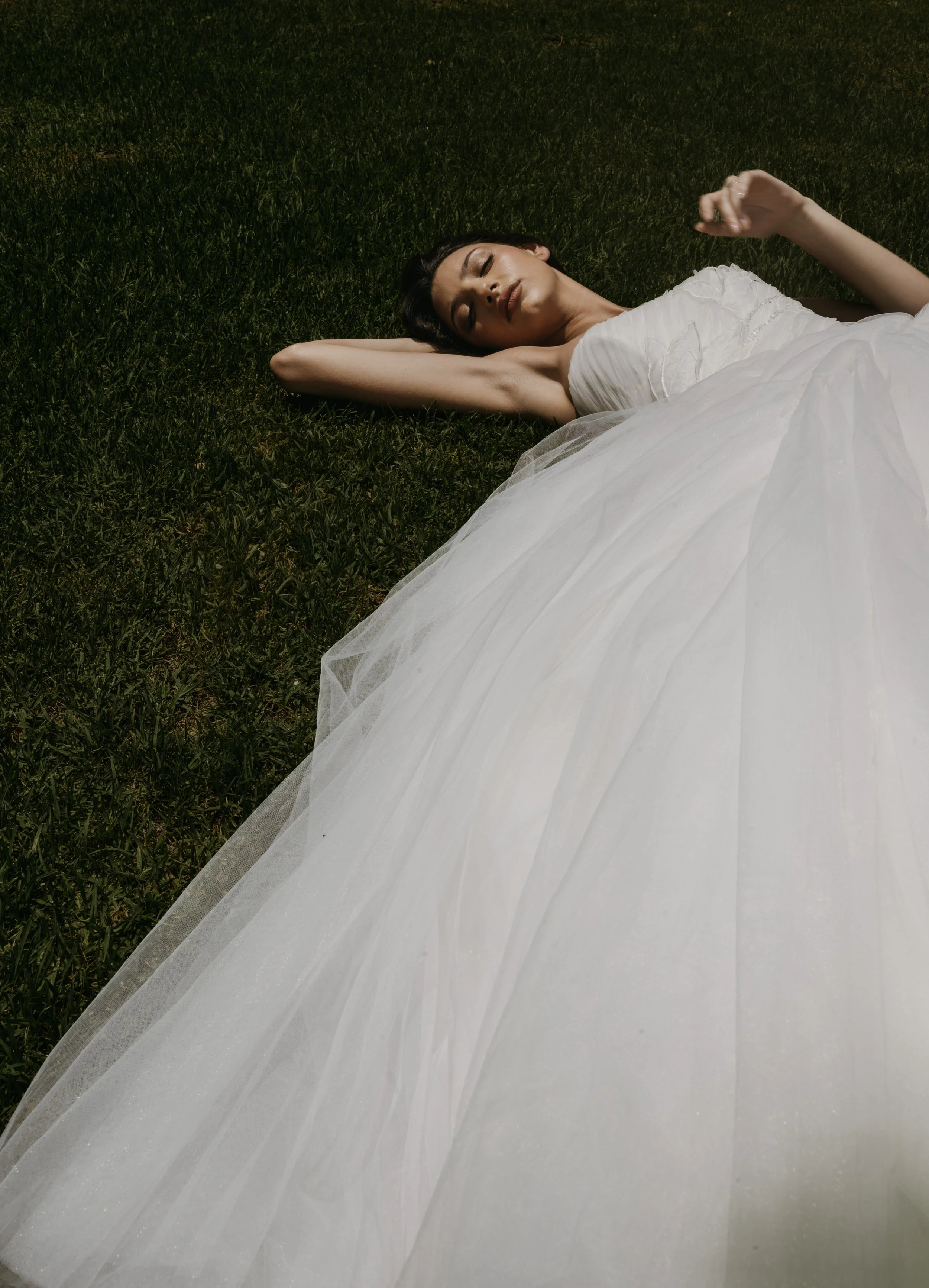 	
Guardiola at New York Bridal Market A woman in a white dress is lying on her back on green grass with her arms behind her head and eyes closed.