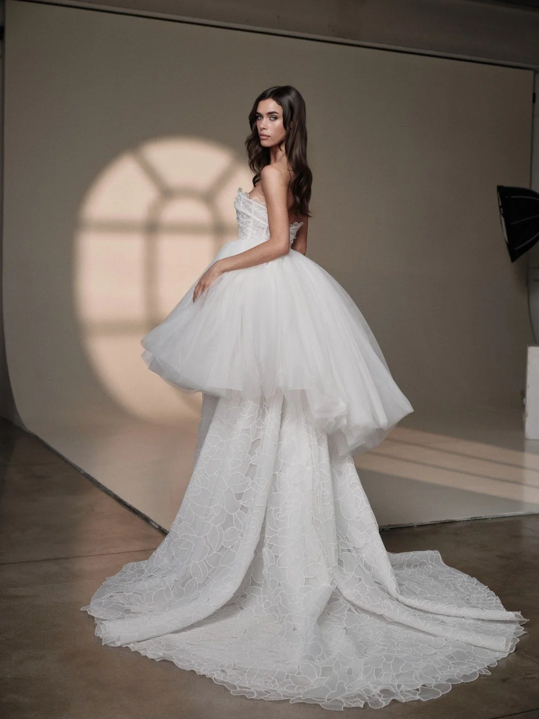 Maria Pia at New York Bridal Market.  A woman in a wedding dress standing in a photography studio with a backdrop and window shadow reflection.
