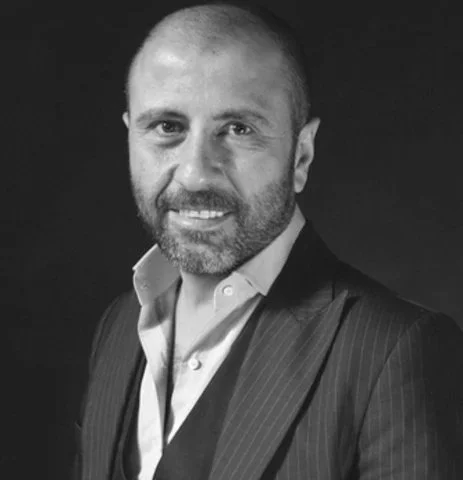 John Paul Ataker at New York Bridal Market. Black and white portrait of a man with a beard, wearing a suit and open-collared shirt