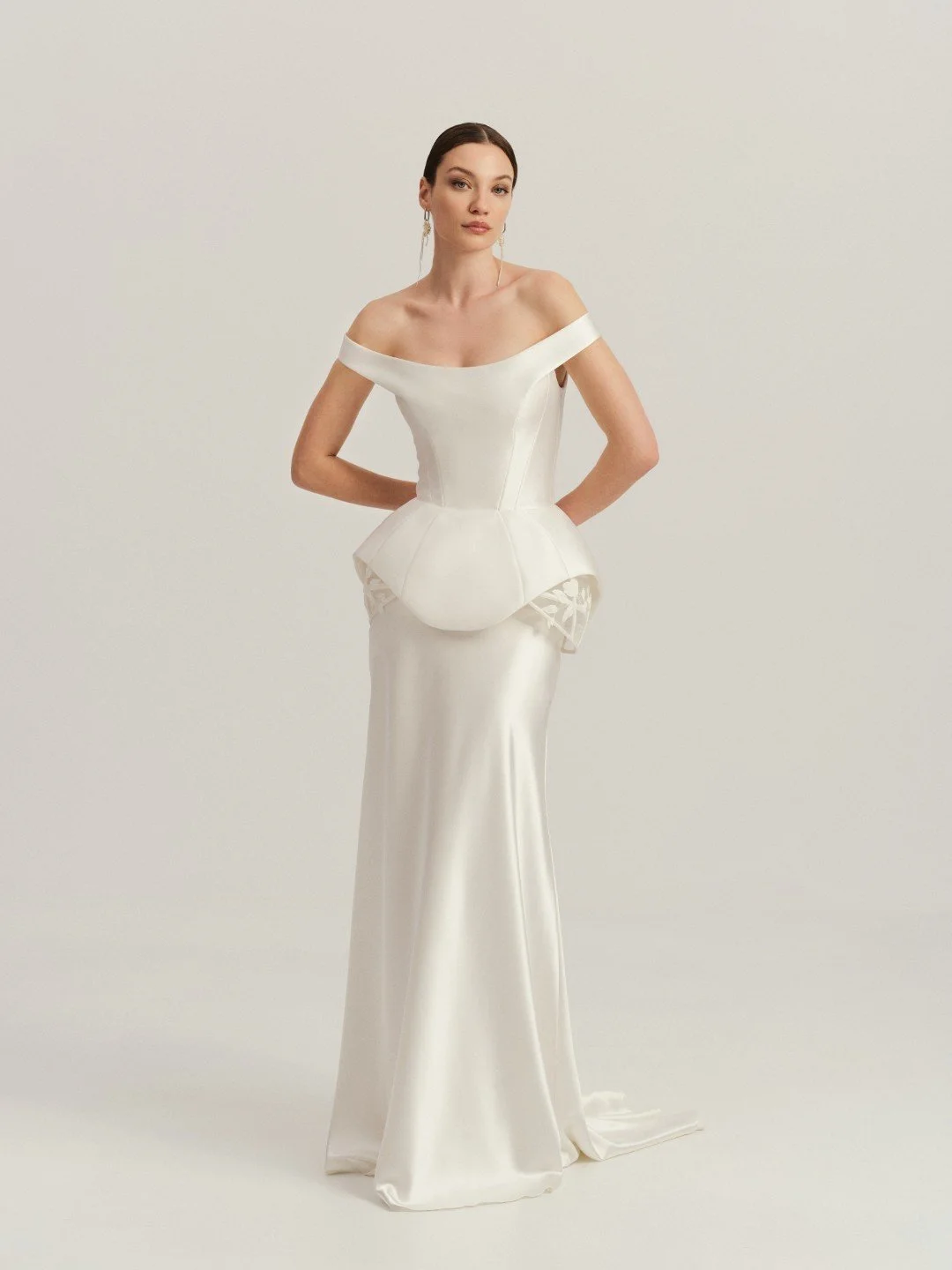 Divine Atelier at New York Bridal Market.  Woman in a white off-the-shoulder gown with a fitted bodice and a long, flowing skirt