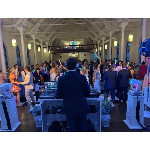 DJ playing music at a lively party in a large decorated hall with many dancing guests.