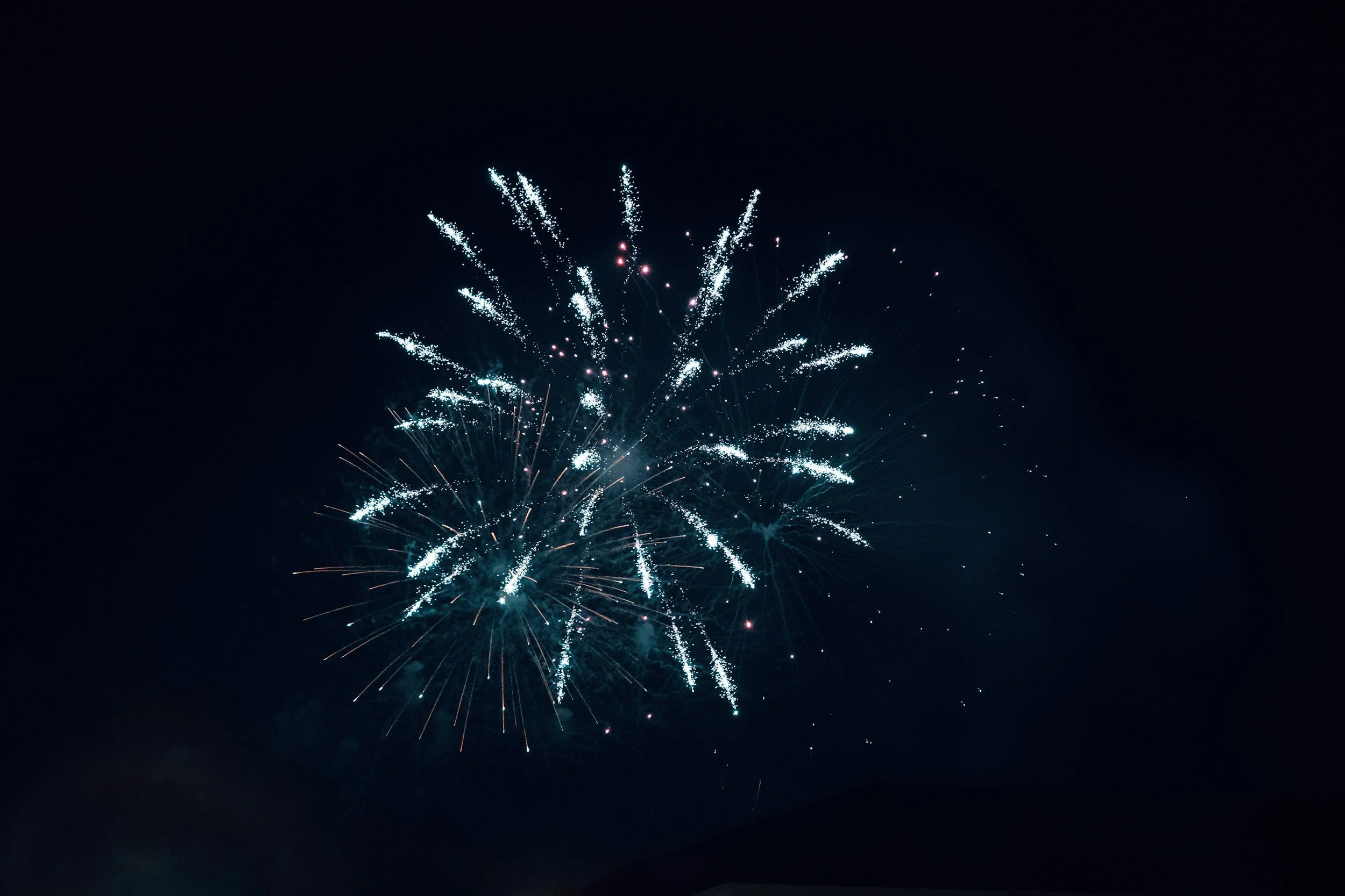 Fireworks exploding in a dark night sky with bright white and blue streaks.