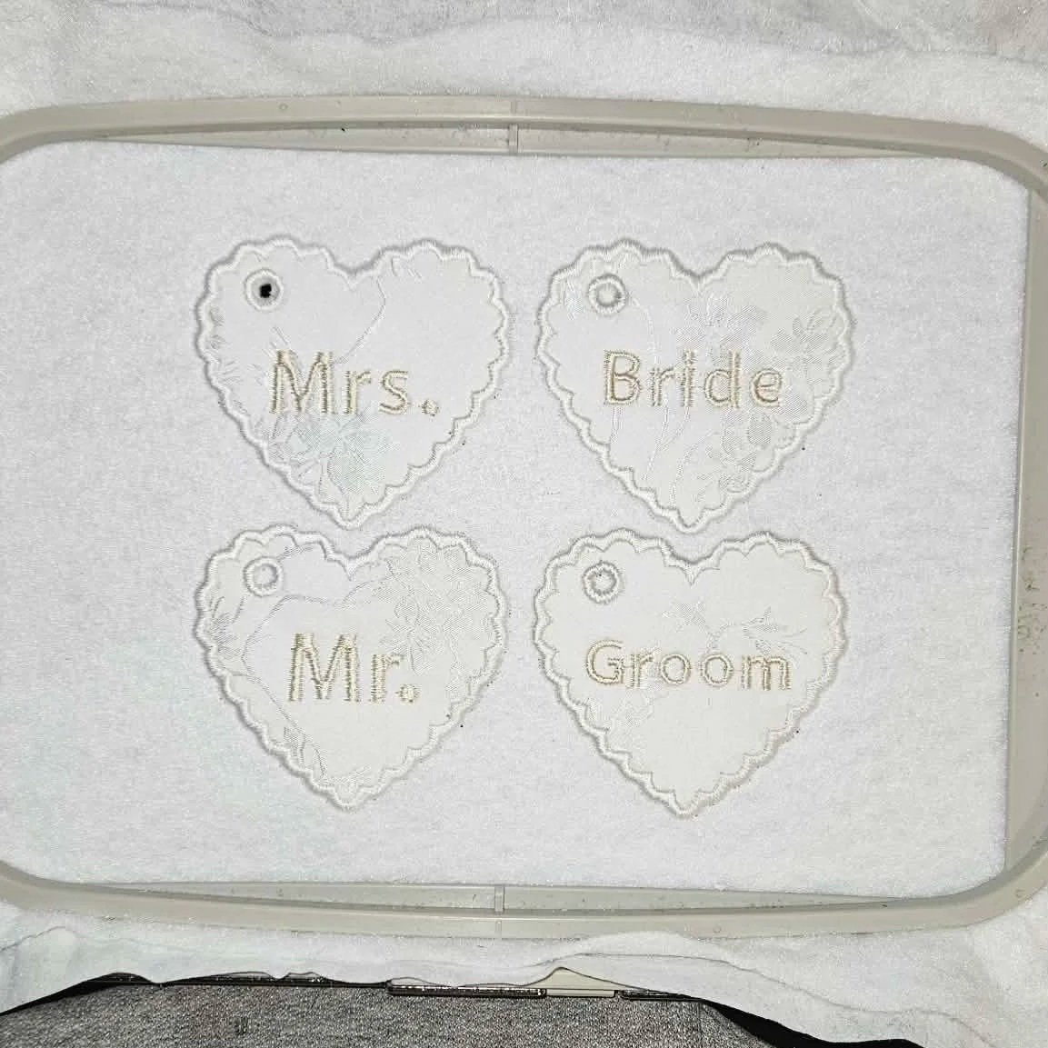 Elegant white heart-shaped wedding tag charms embroidered in rose gold with “Mr.”, “Mrs.”, “Bride”, and “Groom”, perfect for personalized wedding keepsakes and gifts.