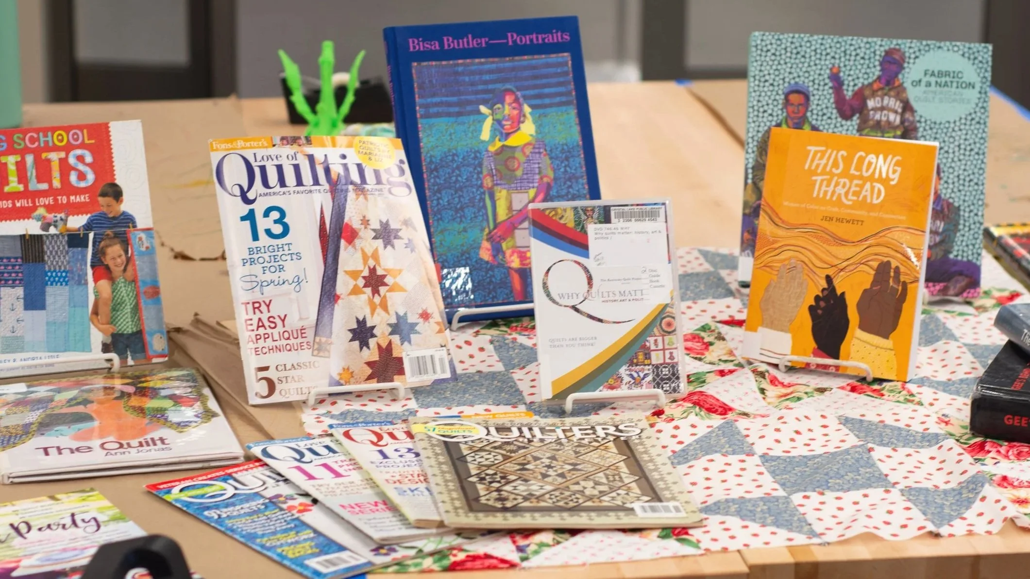 Display of quilting and sewing magazines, pamphlets, and quilting patterns on a table at a craft fair or bookstore.