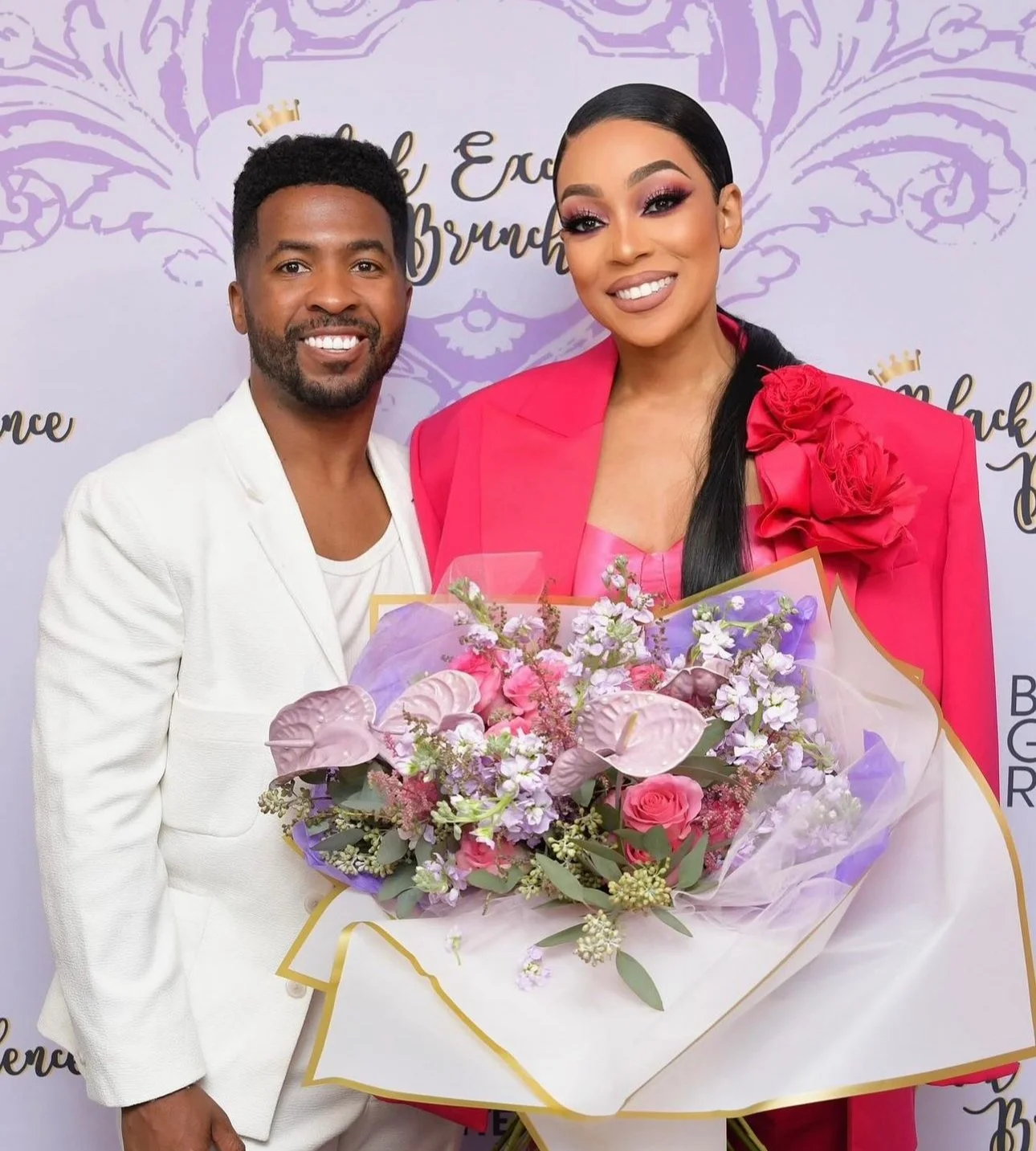 A man and woman smiling, with the woman holding a bouquet of pink and purple flowers, in front of a backdrop with writing and decorative elements.