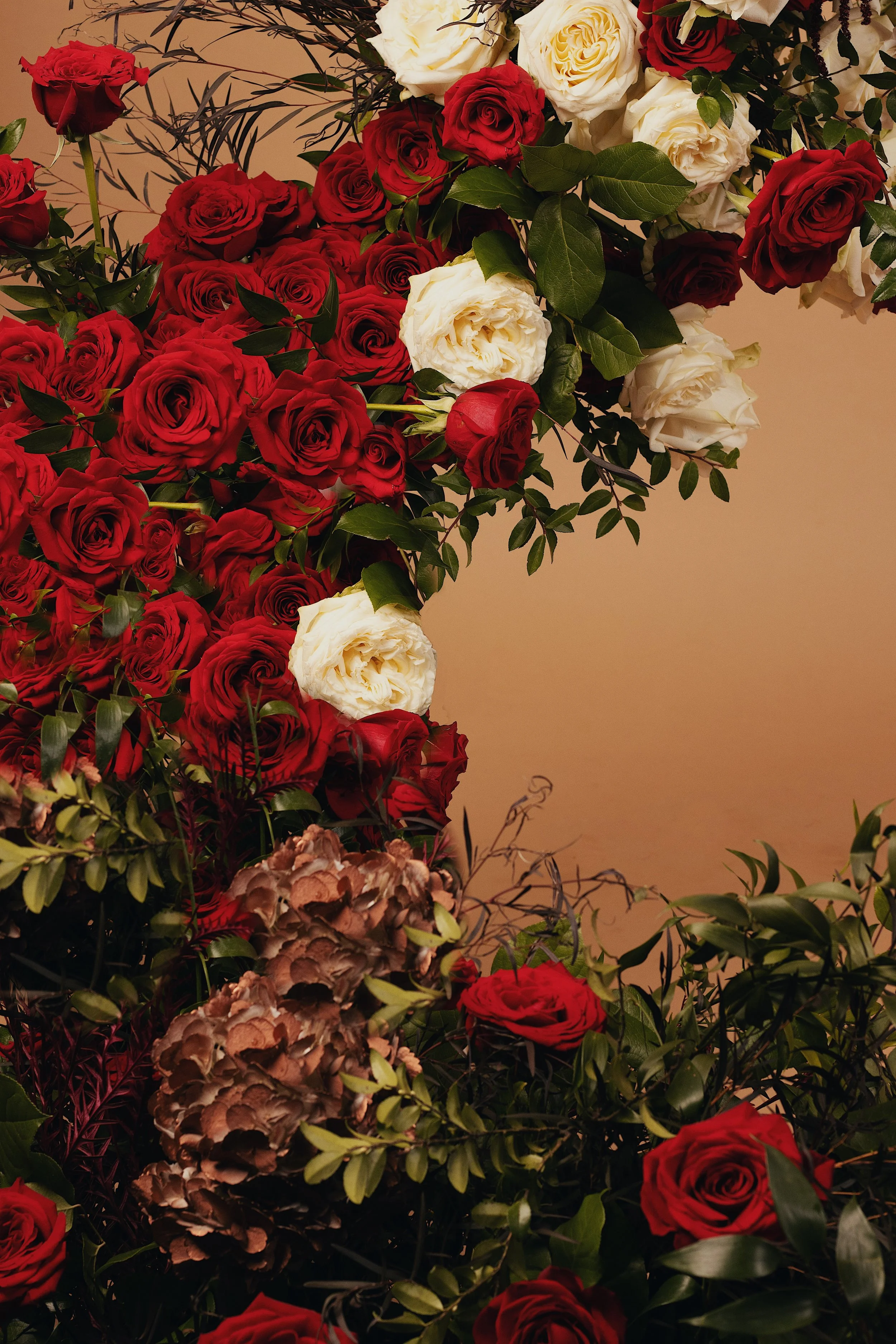 A vibrant floral arrangement featuring red roses, white roses, and brown hydrangeas, accented with green leaves and foliage.