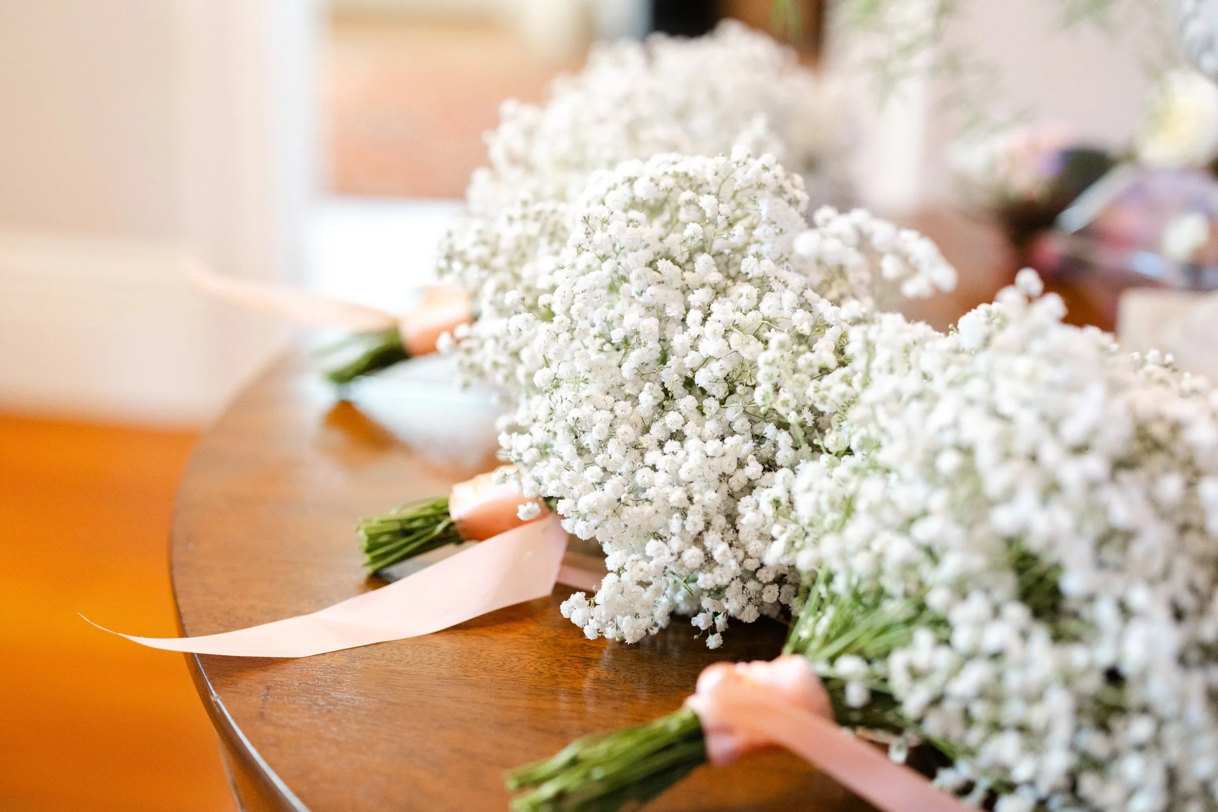 Bouquets of white baby's breath flowers with pink ribbons on a wooden table.