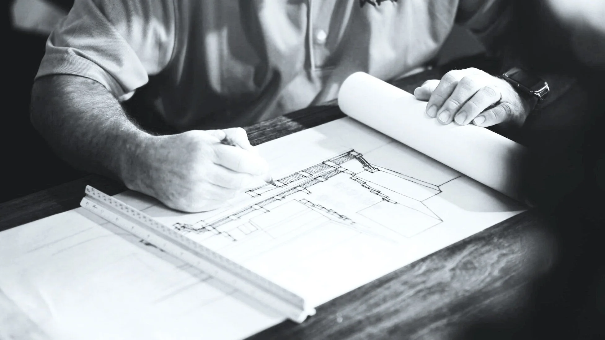 A person reviewing architectural blueprints at a desk, using a ruler for measurements.