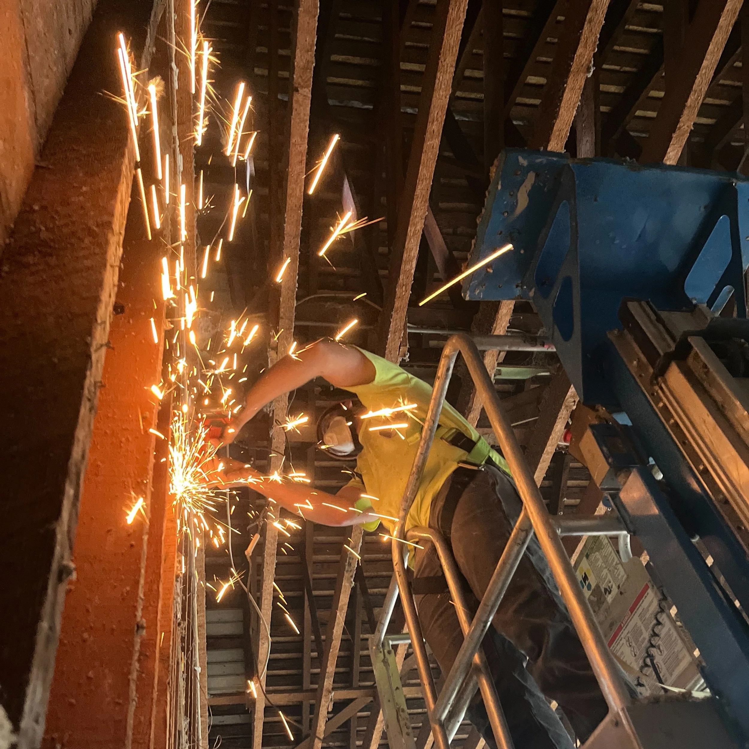 Construction worker welding steel beams with sparks flying inside a building under construction.