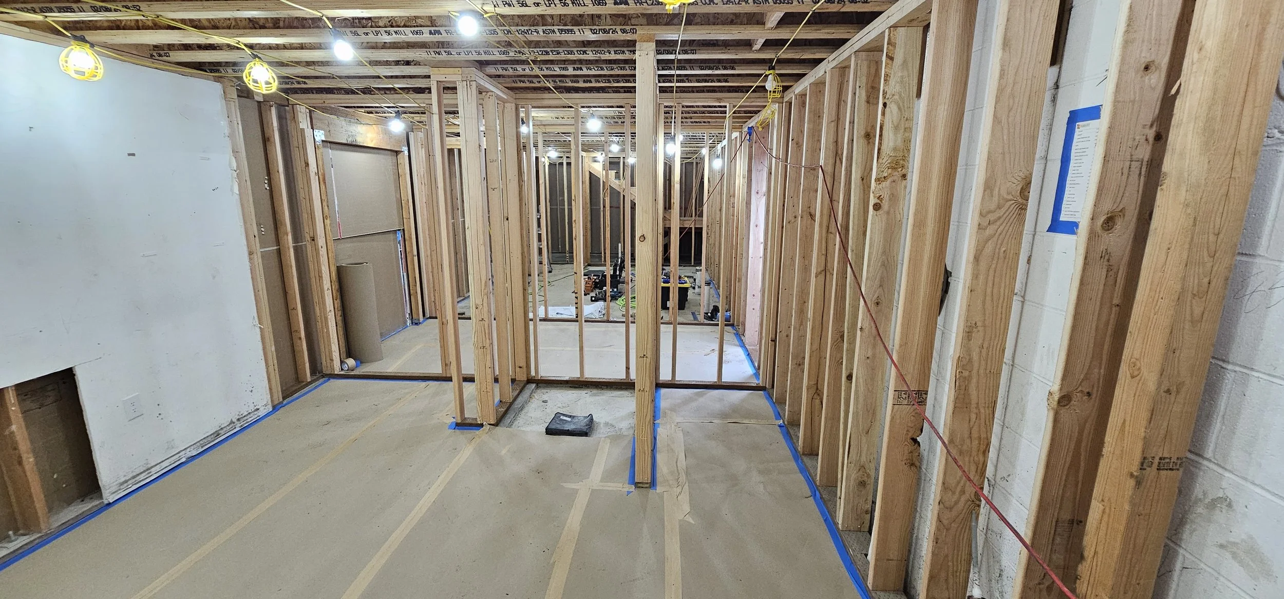 Interior of a house under construction showing wooden framing for walls and ceiling, construction tools, and wiring.