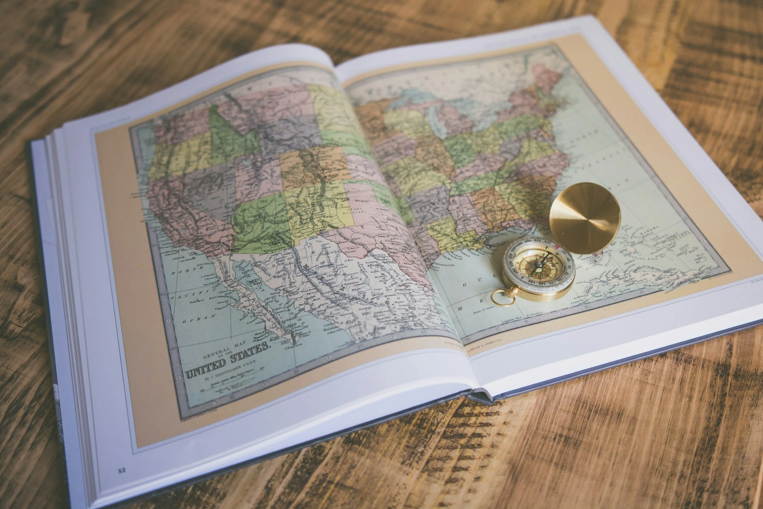 Open vintage map of the United States on a wooden table, with a folded brass compass resting on it.
