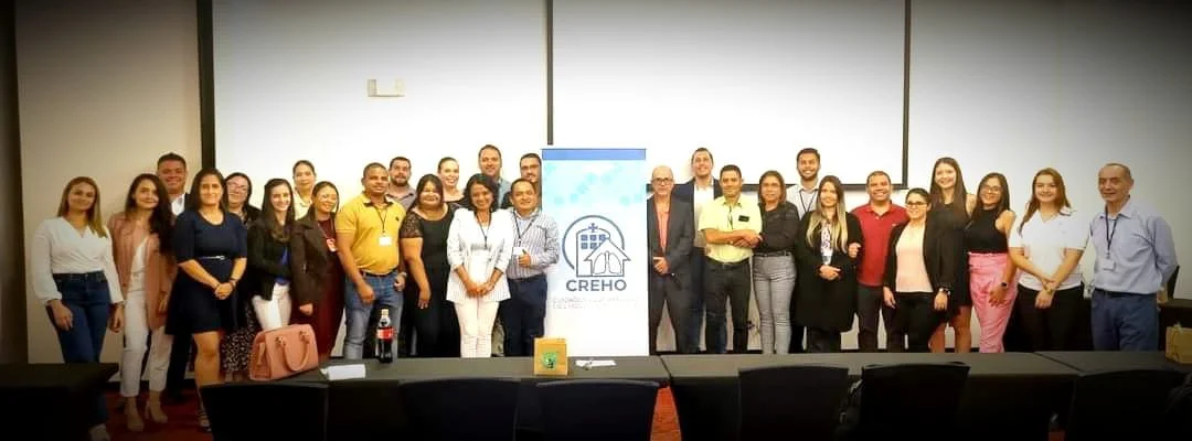 Grupo de personas posando en una sala de conferencias frente a una pantalla y un cartel con el logo de CREHO.