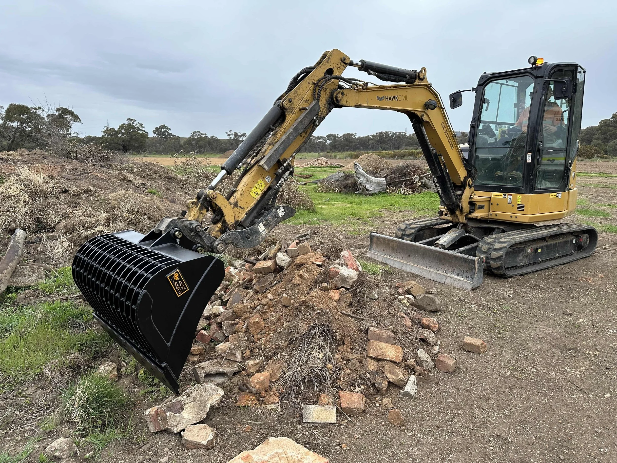 Mini excavator with a black attachment breaking rocks in a field.