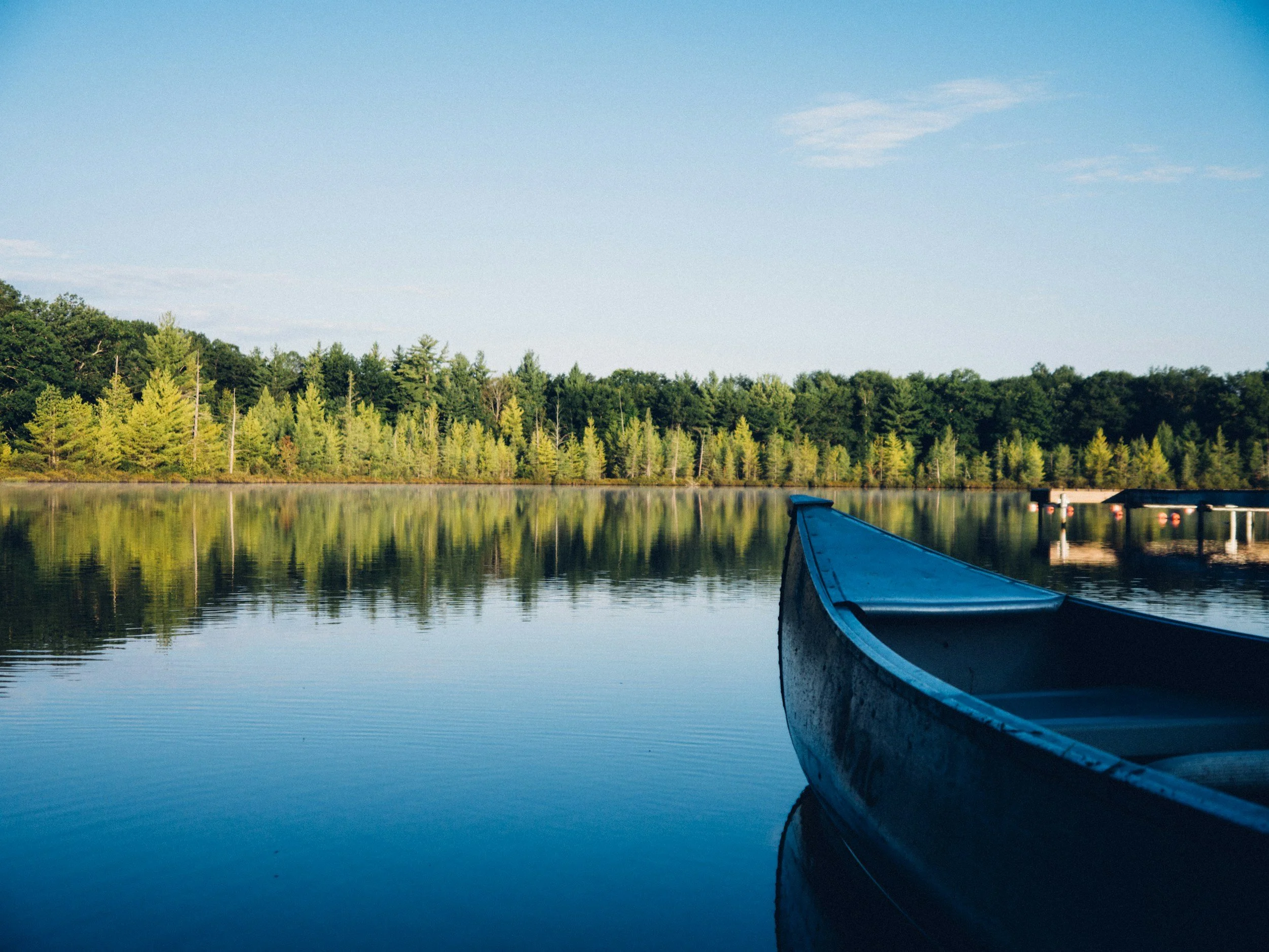 A blue canoe floating on a calm lake with a forested shoreline and a clear blue sky reflected in the water.