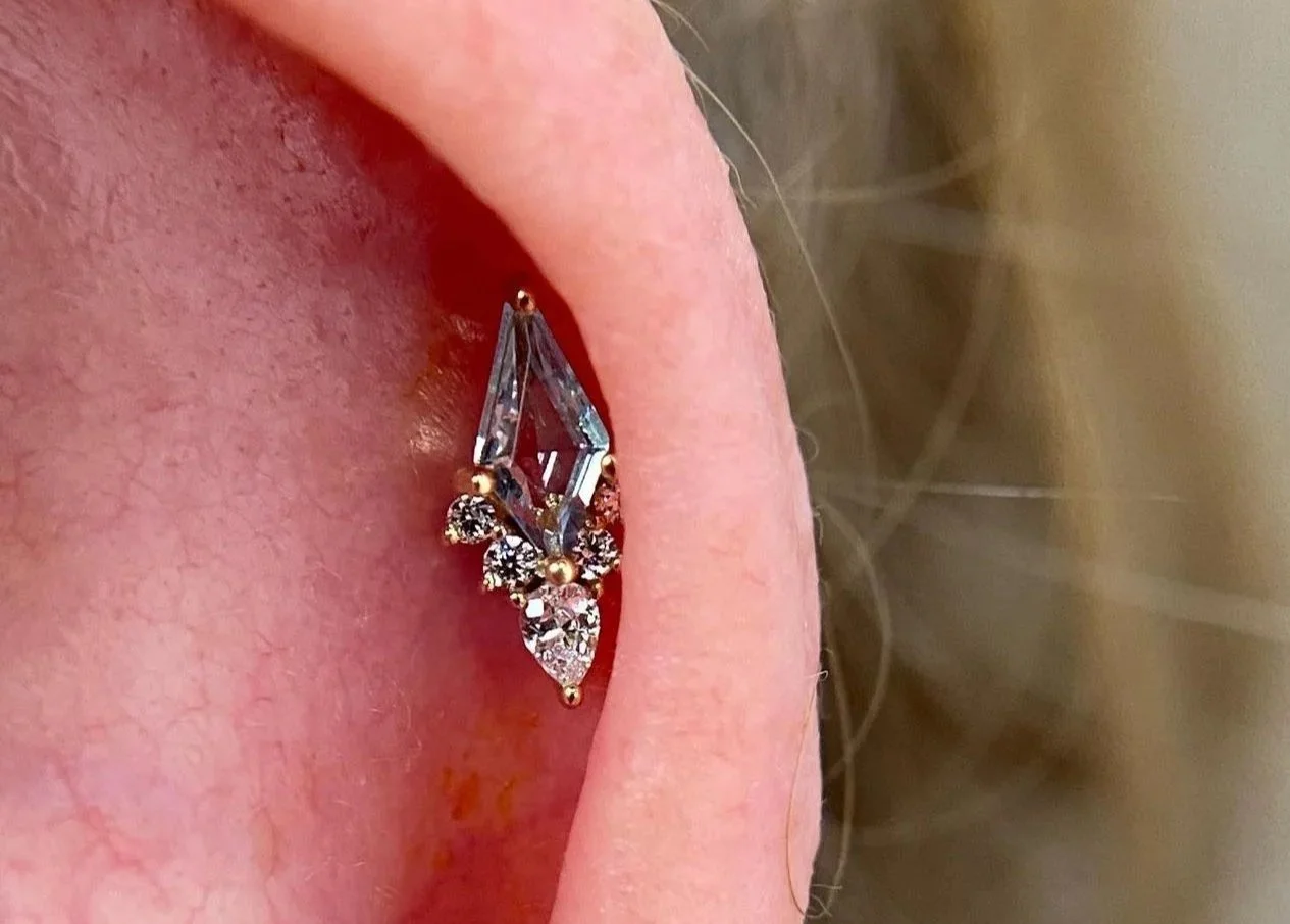 Close-up of a person's ear with a decorative earring featuring a marquise-shaped stone and small surrounding diamonds.