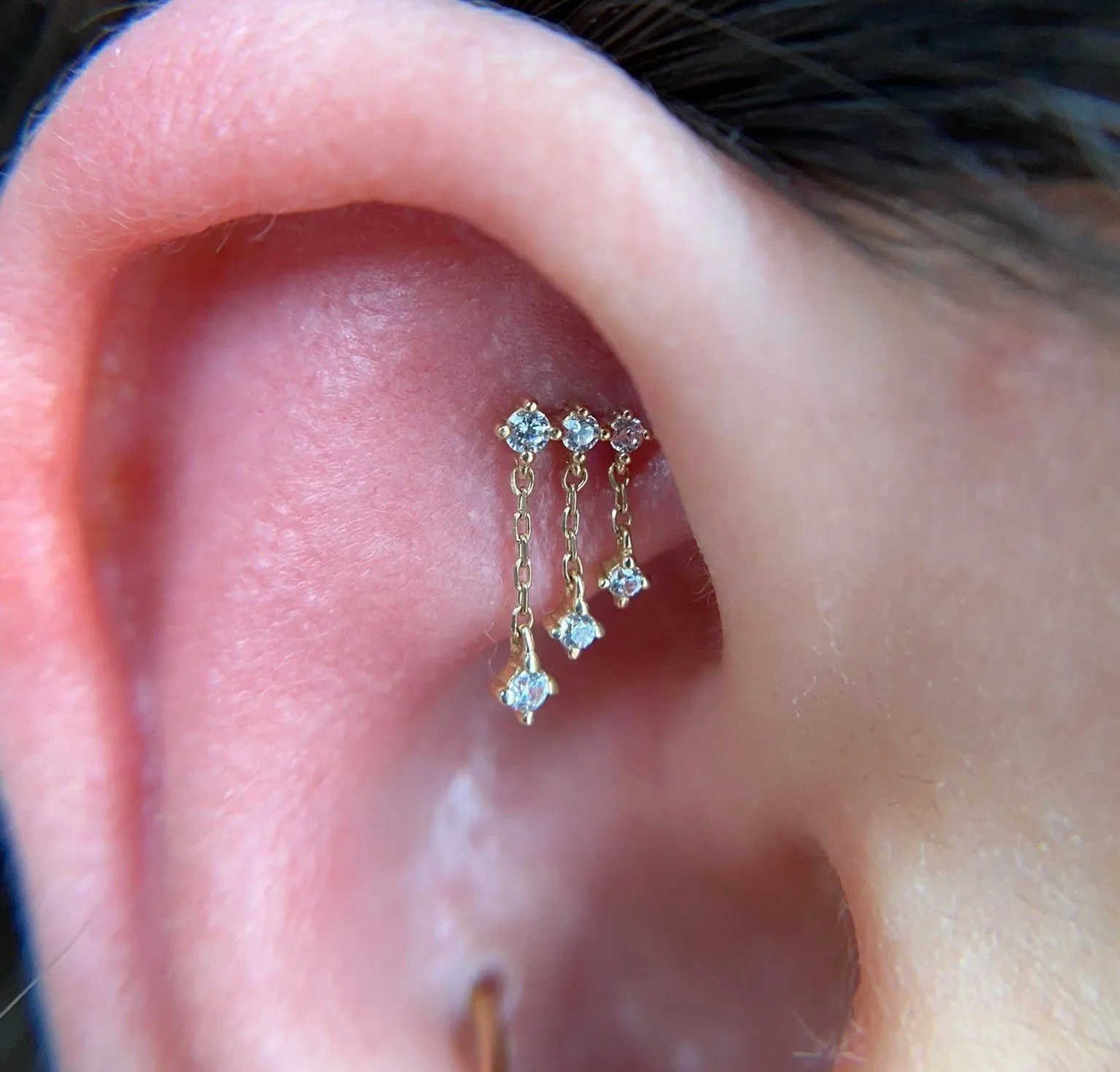 Close-up of a person's ear with multiple earrings, including a gold hoop and a three-stone star-shaped diamond dangling earring.