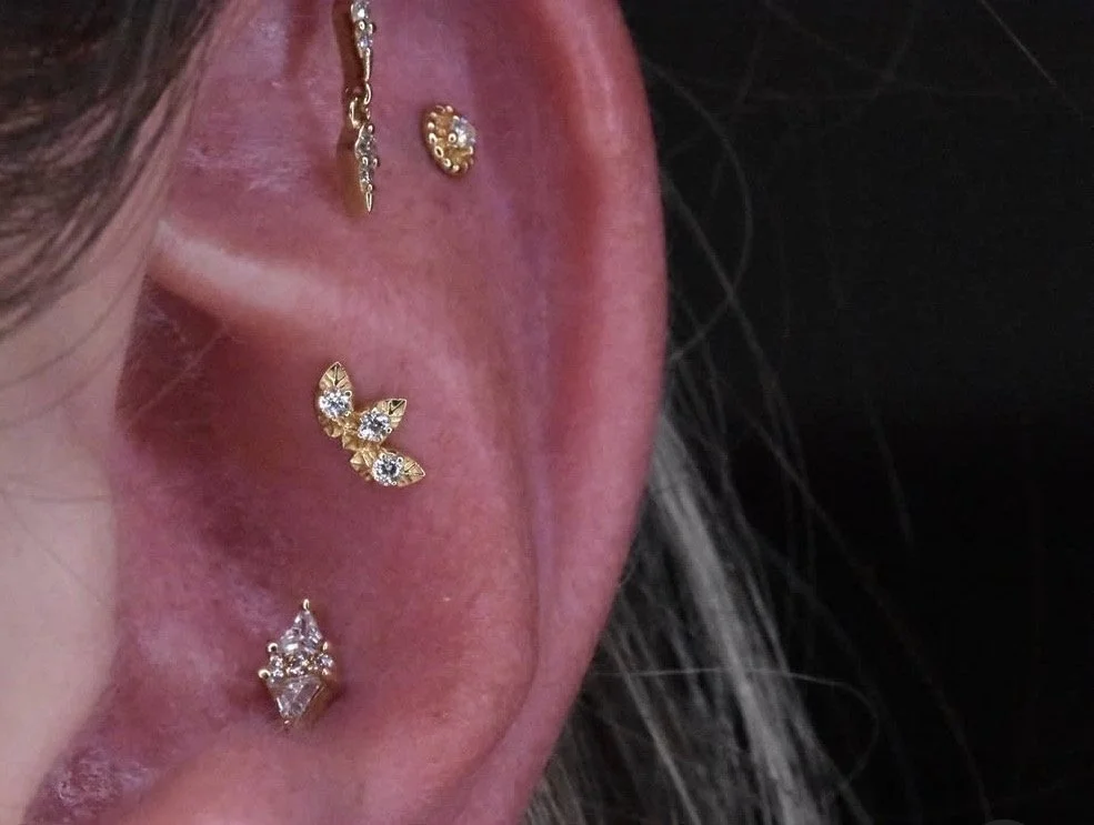 Close-up of a person's ear adorned with multiple earrings, including a butterfly-shaped earring with crystals, a small round crystal stud, and a delicate chain with small charms.
