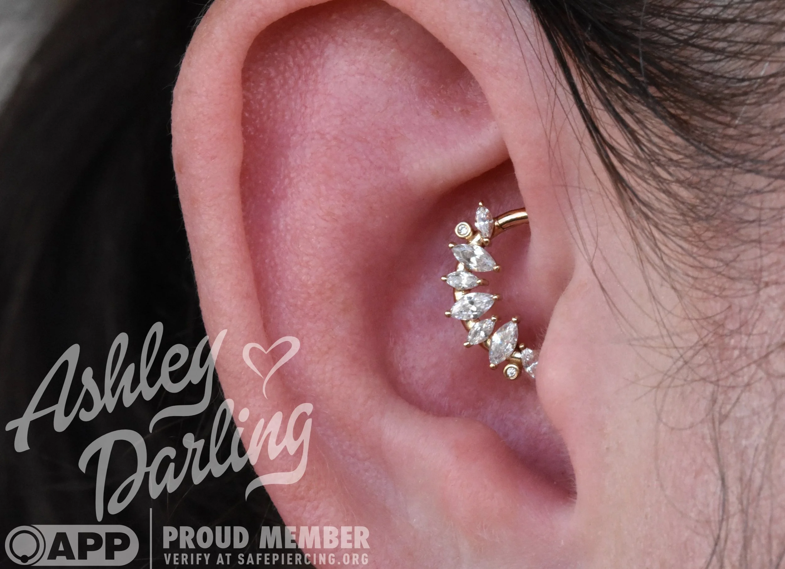 Close-up of a woman's ear with a gold cartilage piercing decorated with a curved row of clear, marquise-cut and round diamonds.