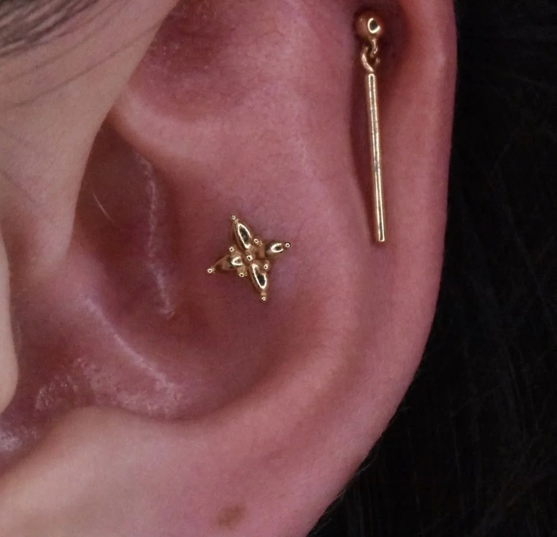 Close-up of a person's ear with two gold earrings: one star-shaped and one straight bar with a small loop.