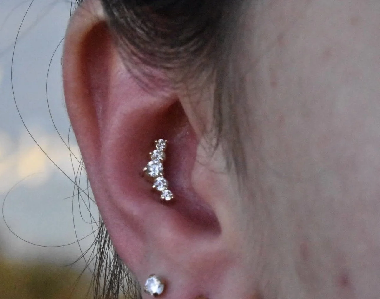 Close-up of a person's ear with multiple diamond-studded piercings, including a helix and lobe piercing.