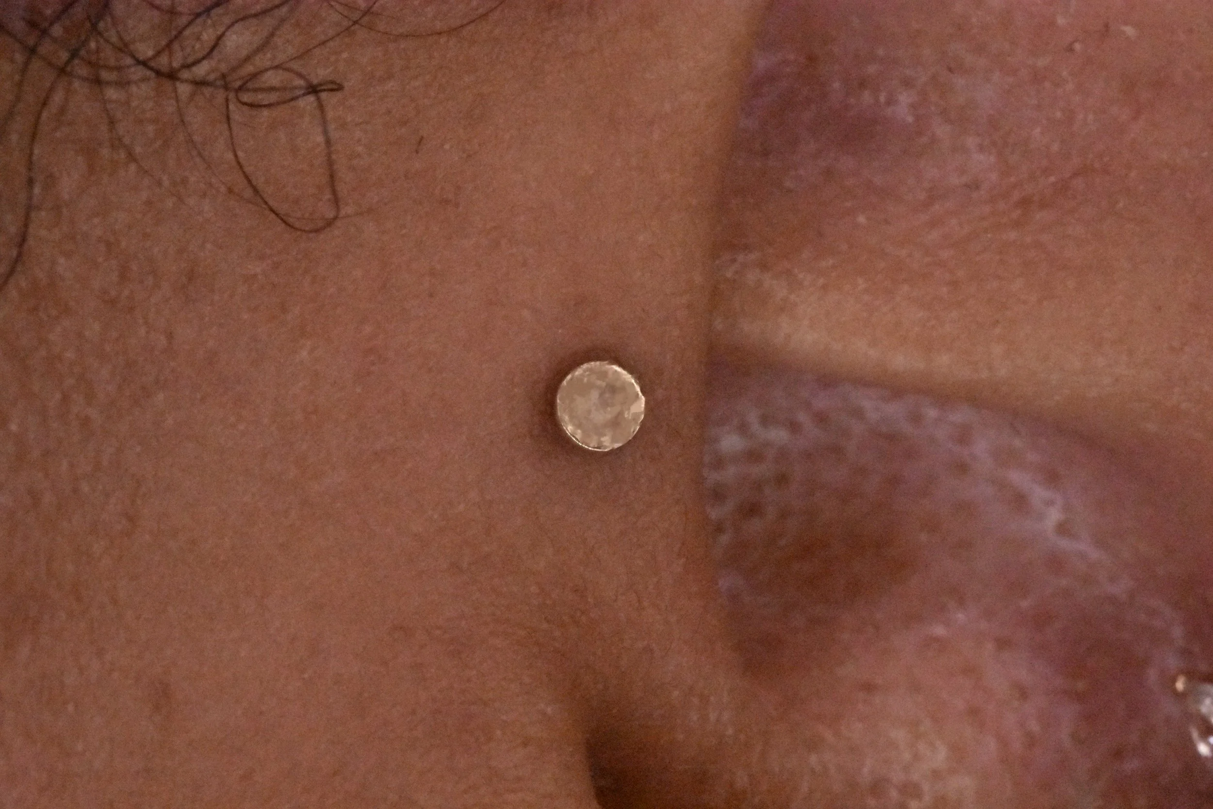 Close-up image showing a person's skin with a coin placed on it, and some hair visible at the top left corner.