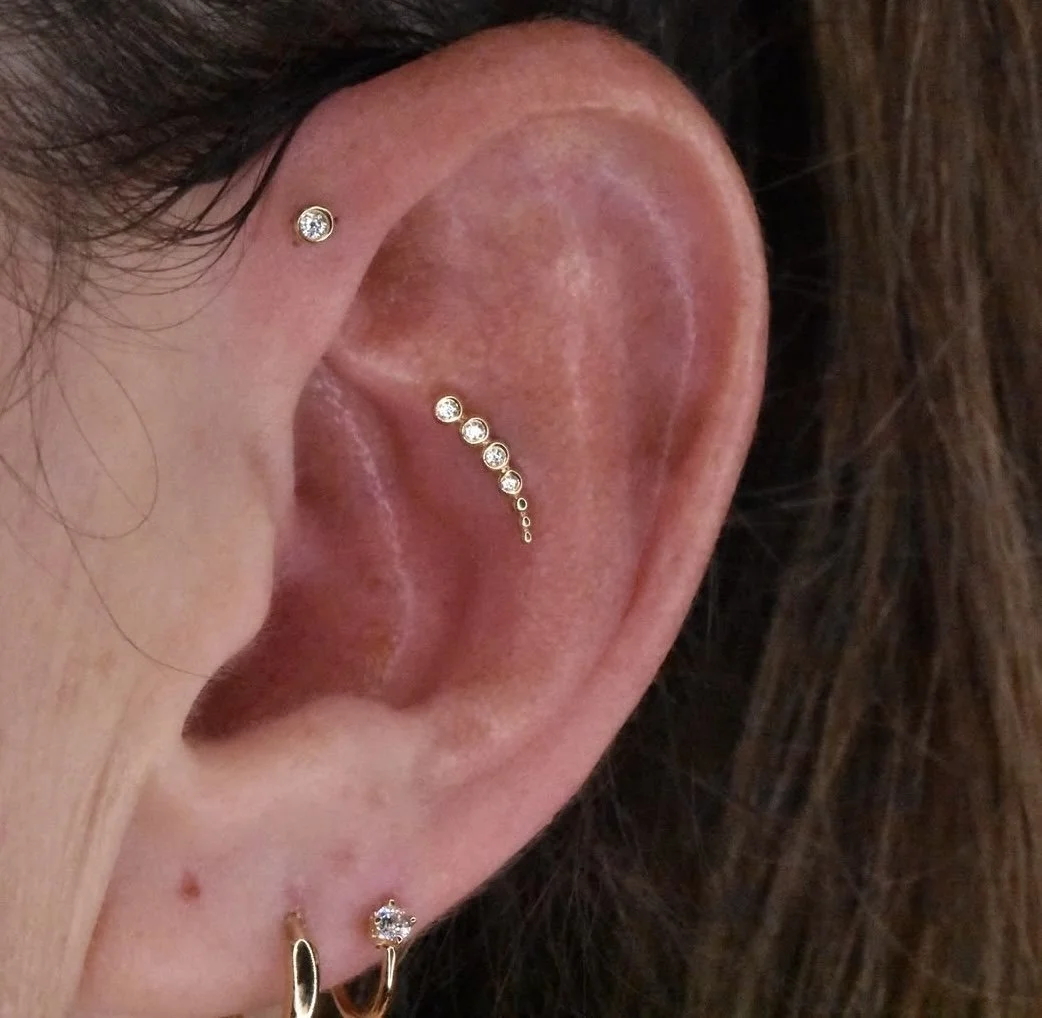Close-up of a person's ear with multiple earrings, including a small stud, a curved line of small diamonds, and a small hoop with a diamond.