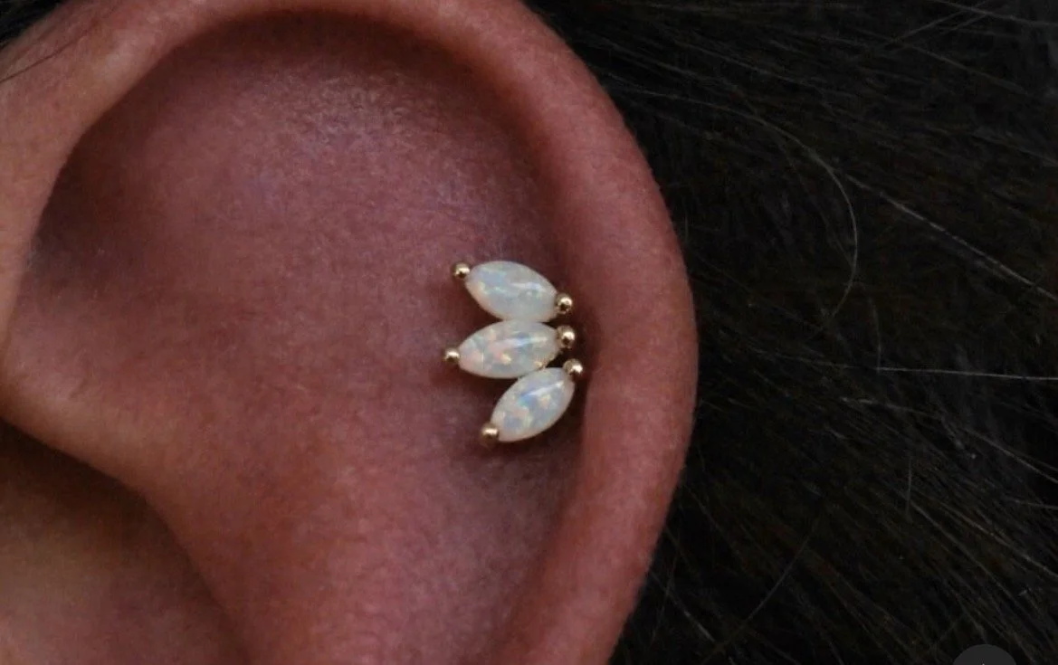 Close-up of a person's ear with a triple opal cartilage earring set in a horizontal line.