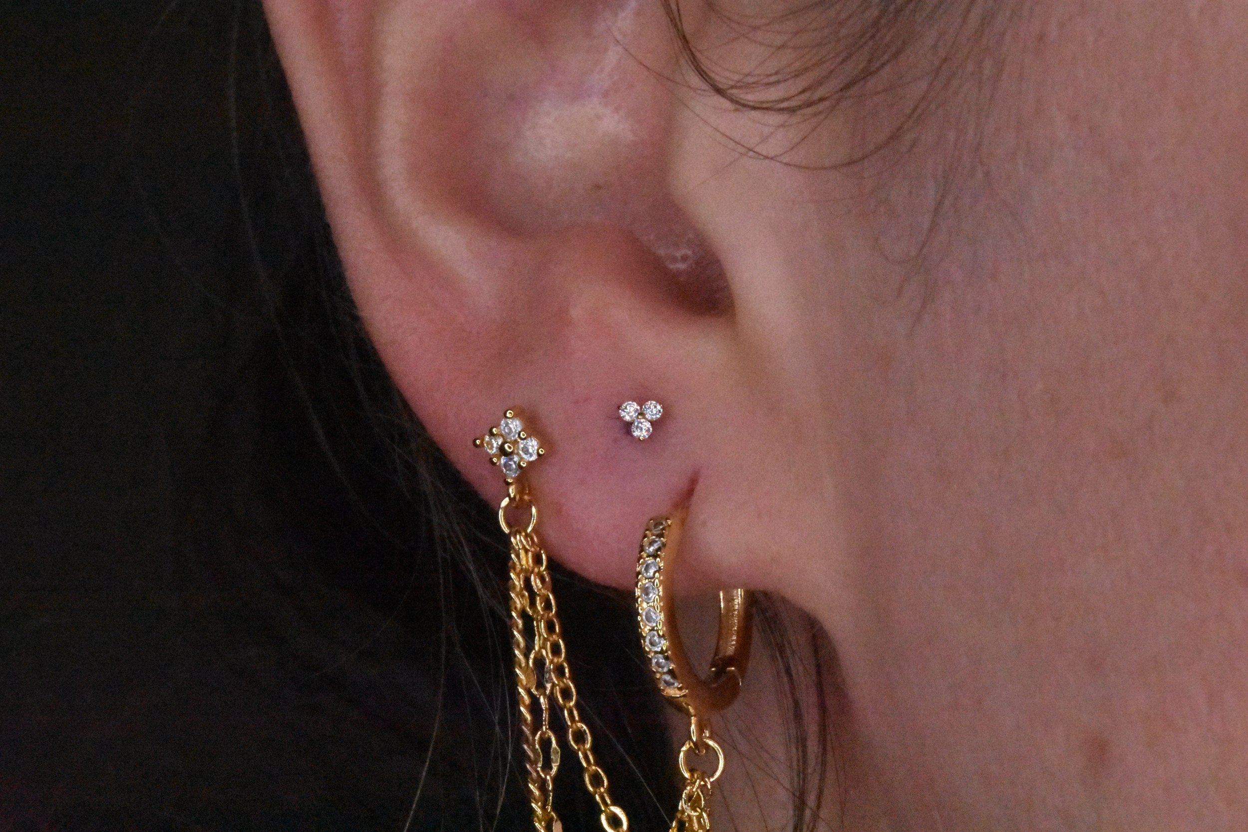 Close-up of a person's ear adorned with multiple gold and diamond jewelry earrings and chains, with dark hair partially visible.