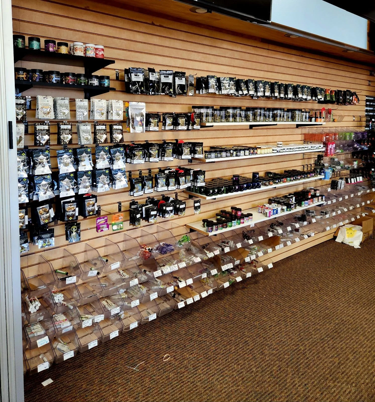 Display of various packaged products in a retail store with shelves containing jars, bags, and small items in plastic containers.