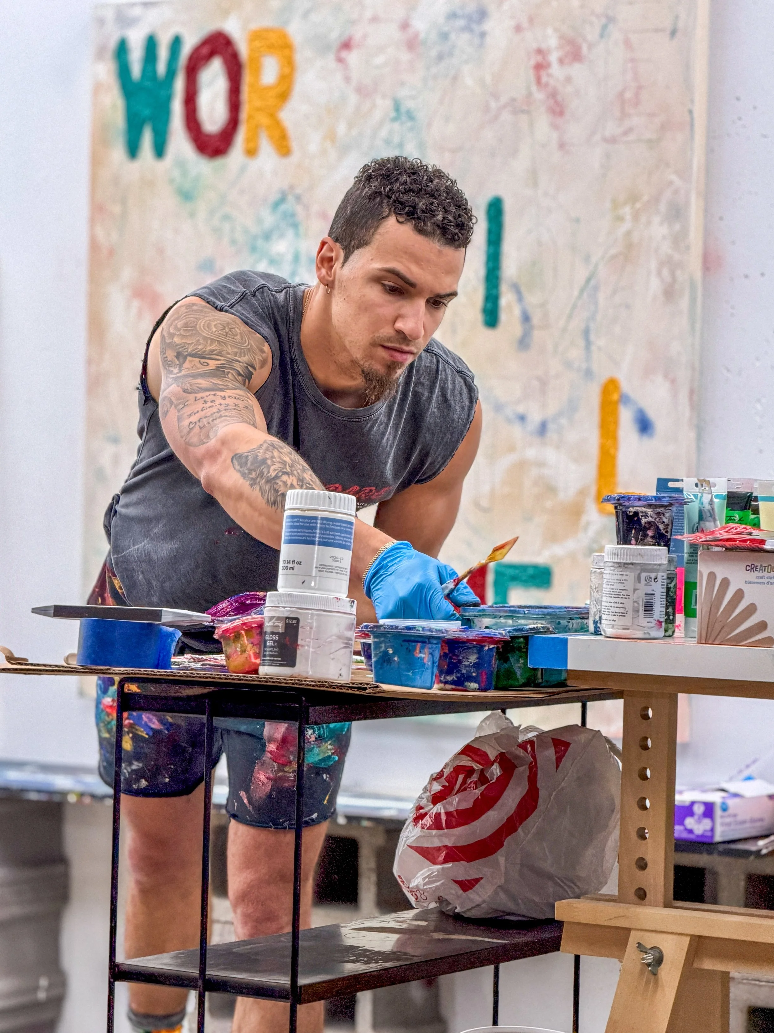 Artist working in studio with text art painting behind him