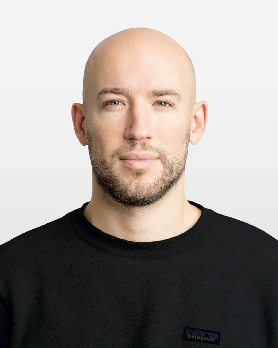 Porträt eines lächelnden Mannes mit Glatze und Bart, trägt ein schwarzes Patagonia-T-Shirt, vor weißem Hintergrund.