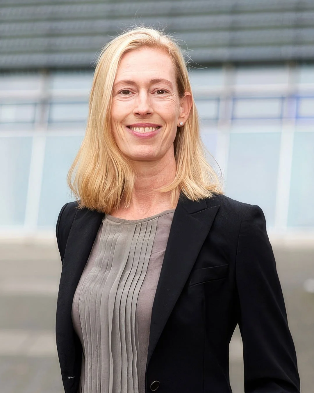 Porträt einer lachenden Frau mit blonden Haaren in einem schwarzen Blazer auf einem modernen Bürofoto