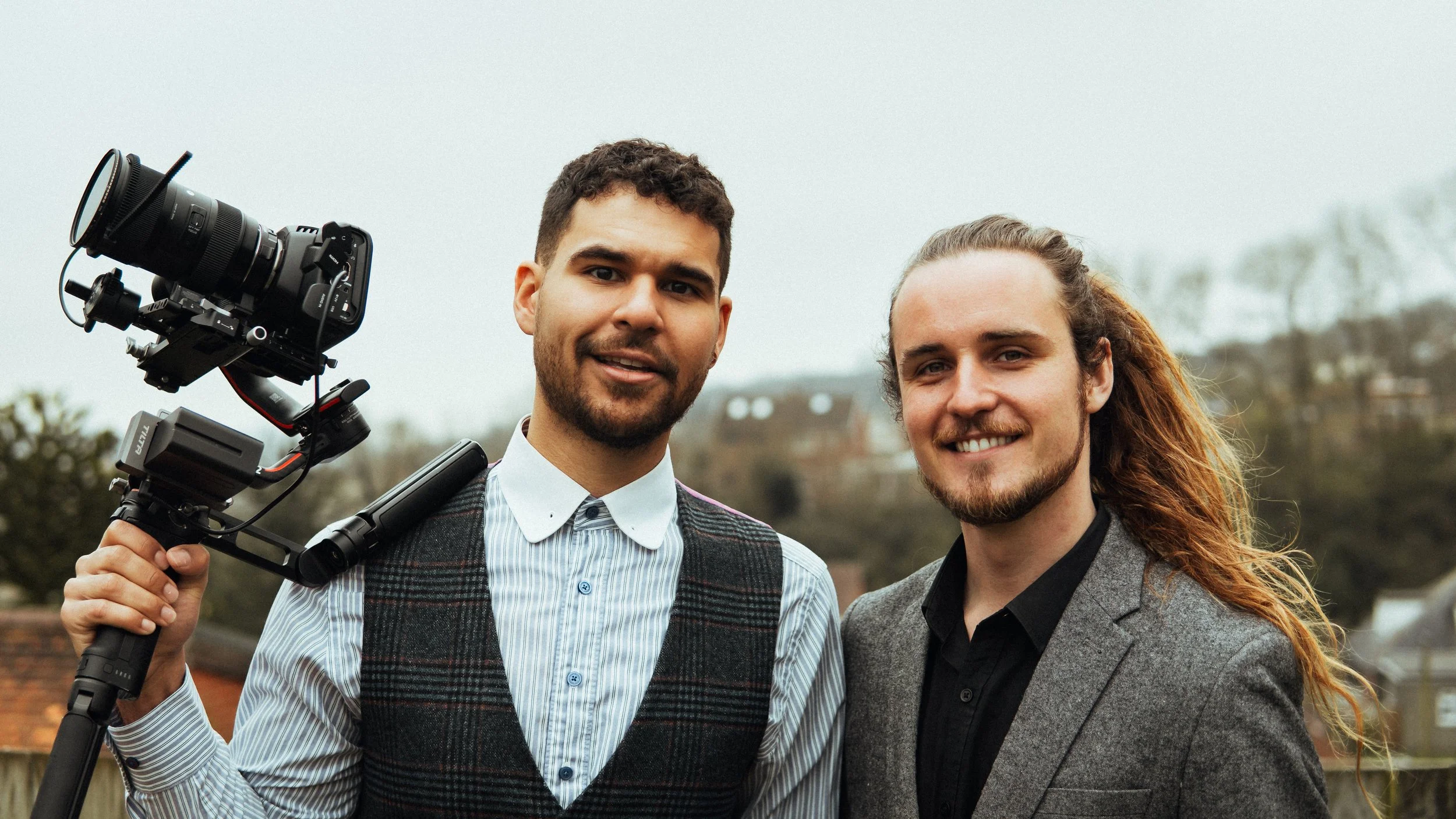 Reece Forward and Jarrod Piner from FFWD Film standing outdoors, one holding a professional camera on a stabilizer, smiling at the camera.