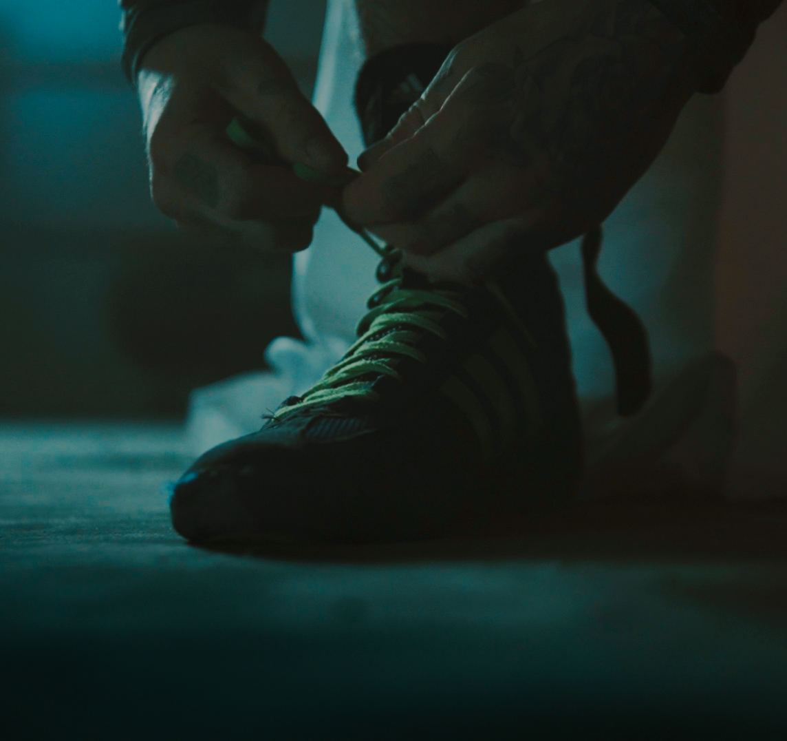 Person tying shoelaces on a sneaker in low light.