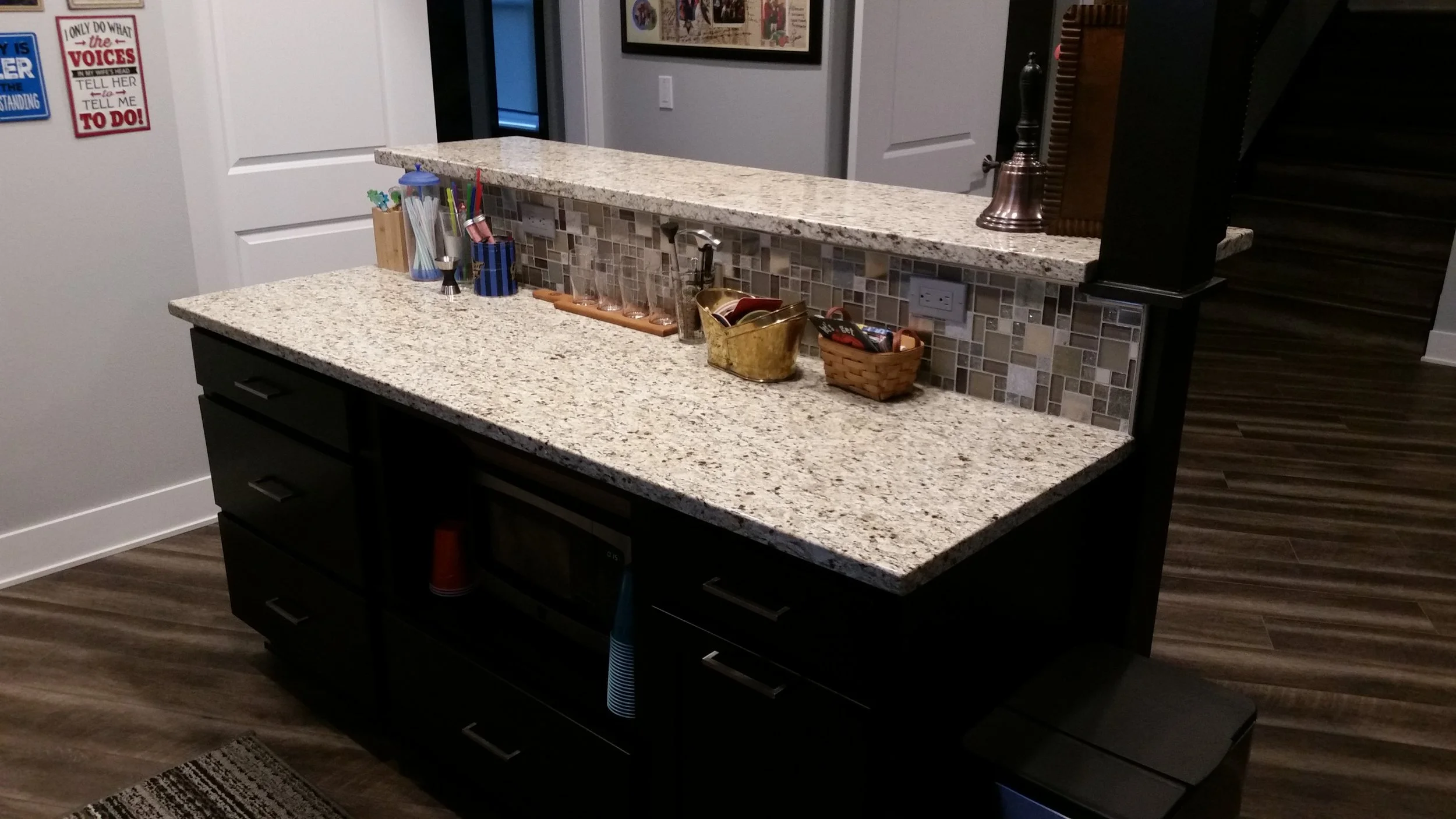 Kitchen with granite countertop, mosaic tile backsplash, black cabinets, and various small decorative items.