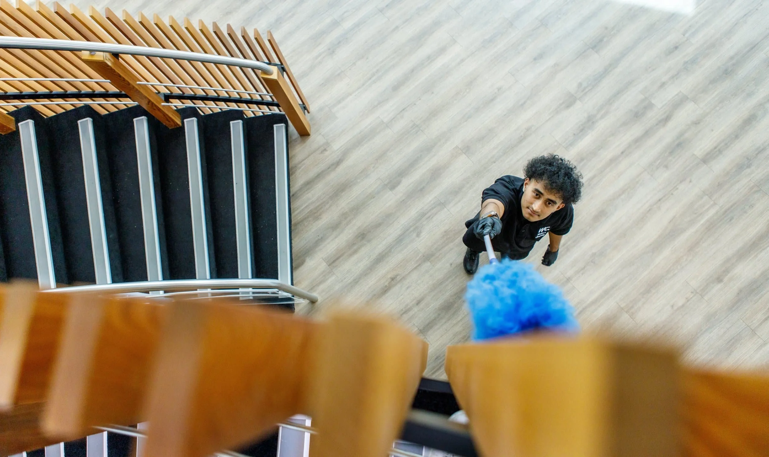 Young man cleaning a staircase with a duster, viewed from above.