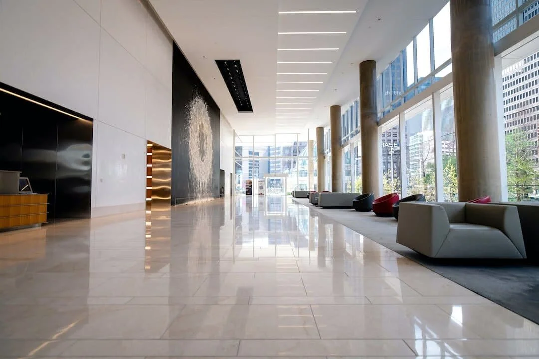 Modern spacious lobby with large floor-to-ceiling windows, high ceiling, marble flooring, and contemporary furniture.