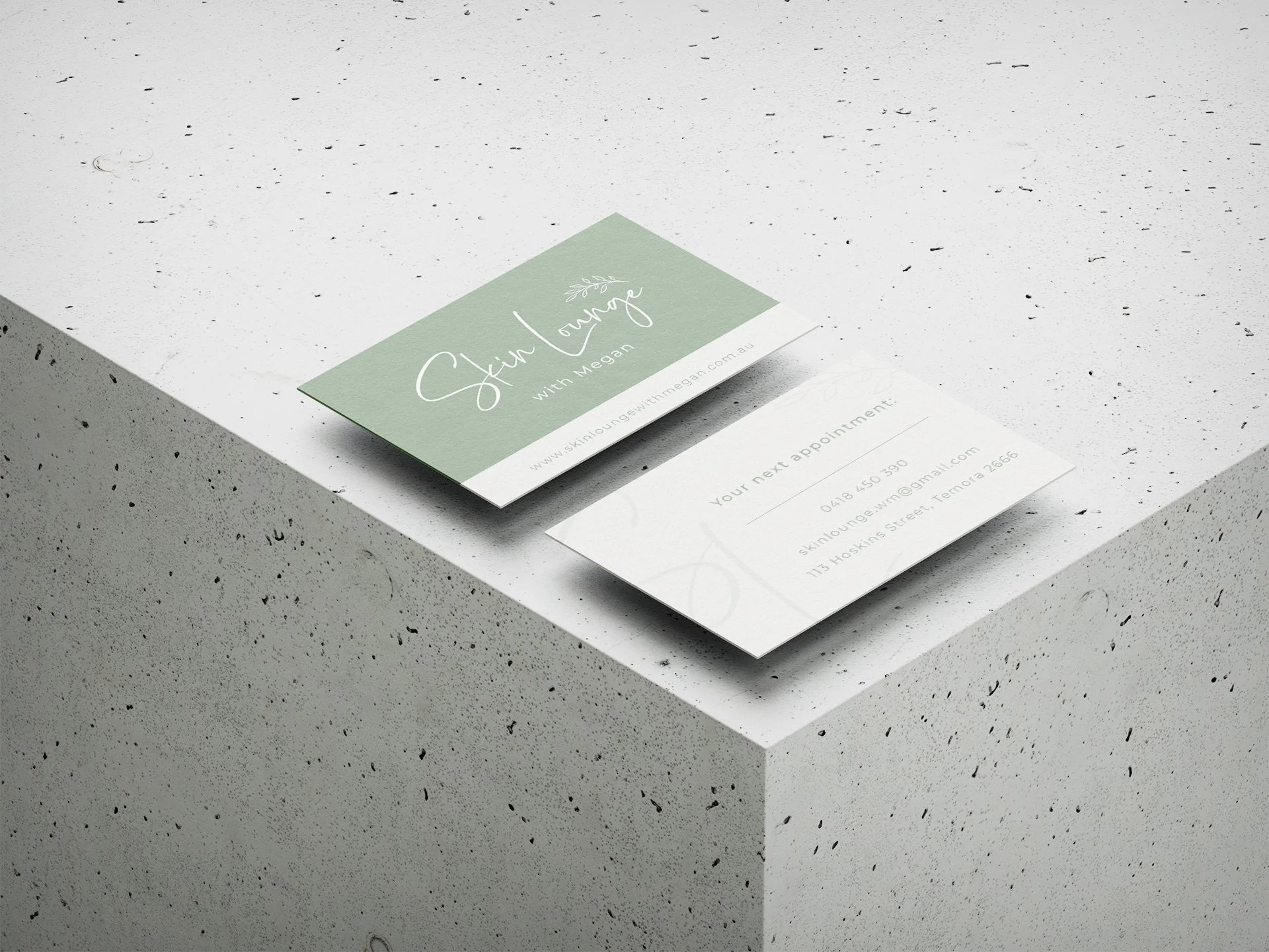 Close-up of a business card for 'Skin Lounge with Megan' placed on a speckled white and grey surface.