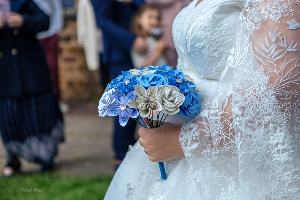 A bride showcases her blue and white bouquet, beautifully framed by a wedding photographer.