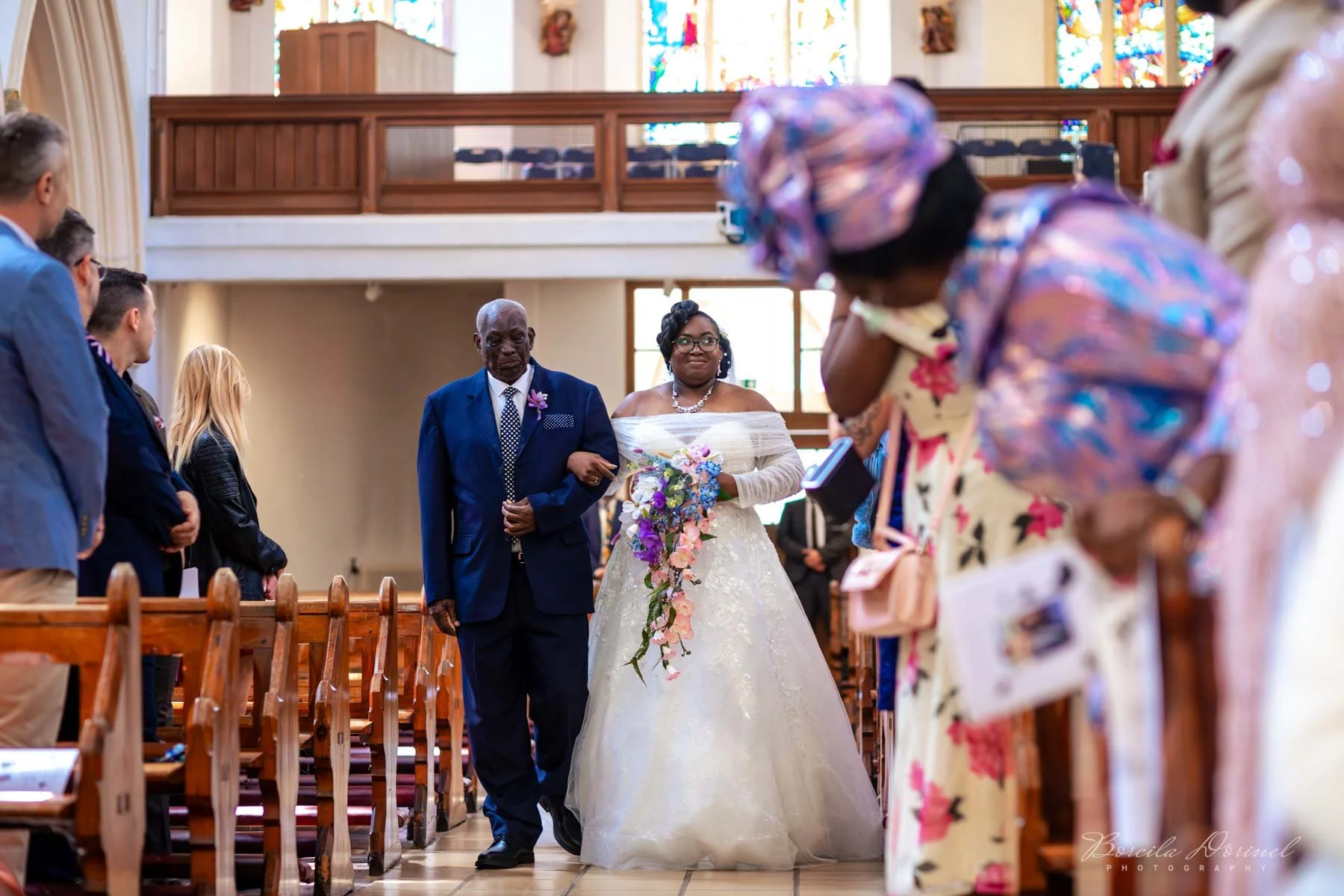 A bride walking down the aisle with her father inside a church, surrounded by family and friends.