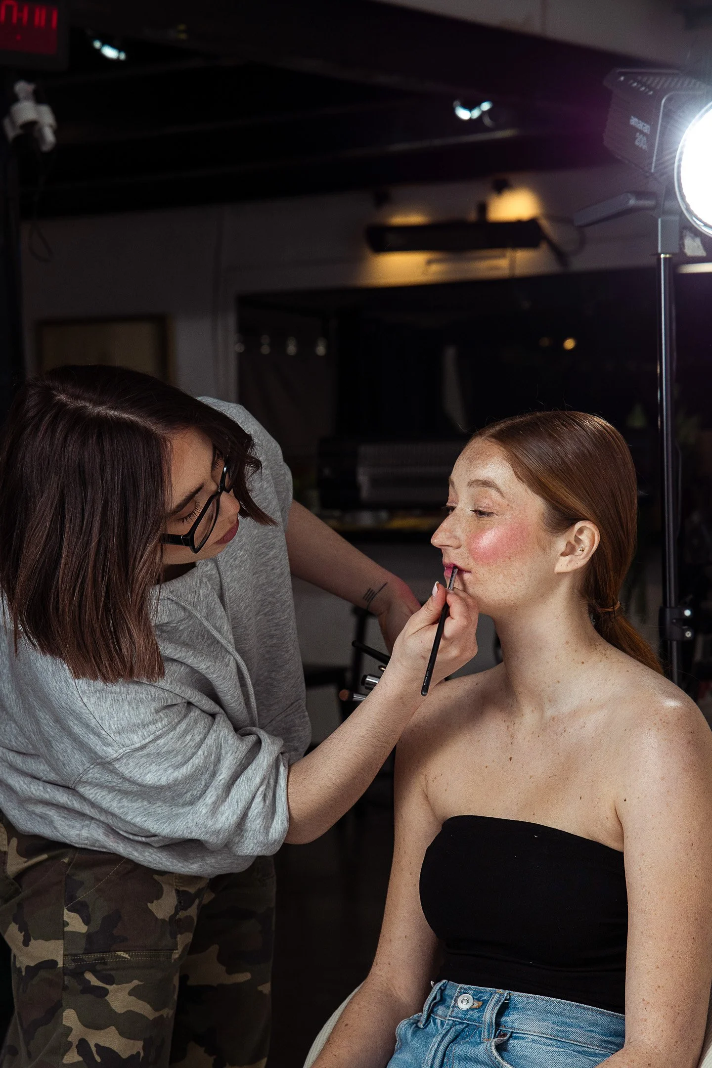Une femme se fait maquiller les lèvres par une autre femme dans un studio de maquillage ou de photographie.
