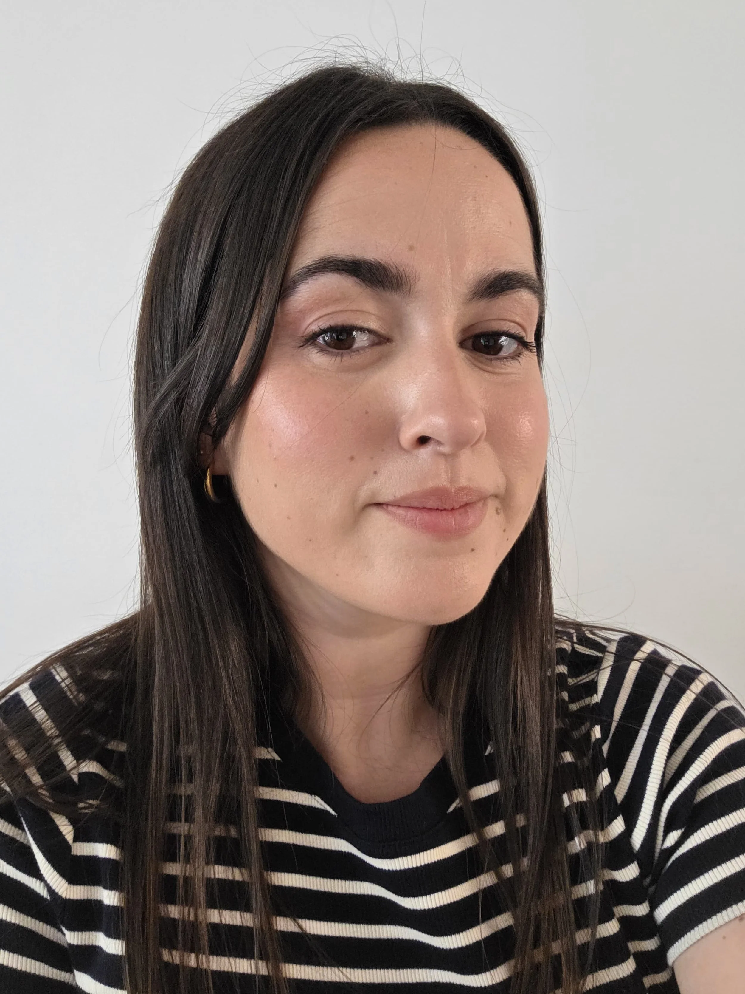 Une femme avec des cheveux longs et noirs, portant un pull à rayures noires et blanches. Son maquillage est lumineux et très naturel.
