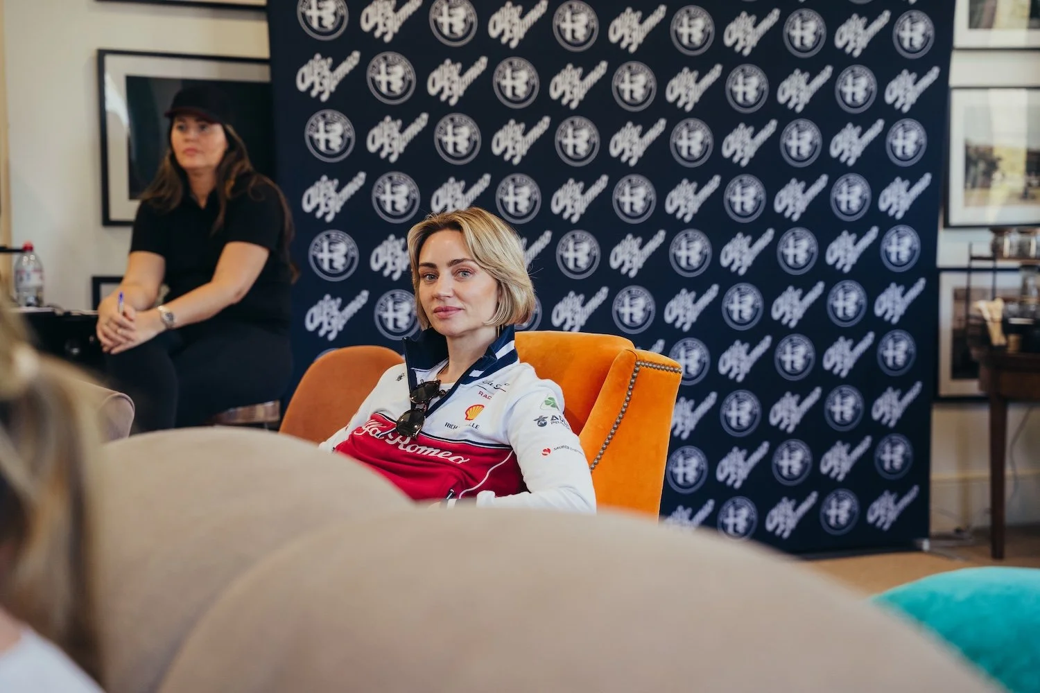 Woman with blonde hair wearing a racing jacket sitting in an orange armchair during a she's on track event