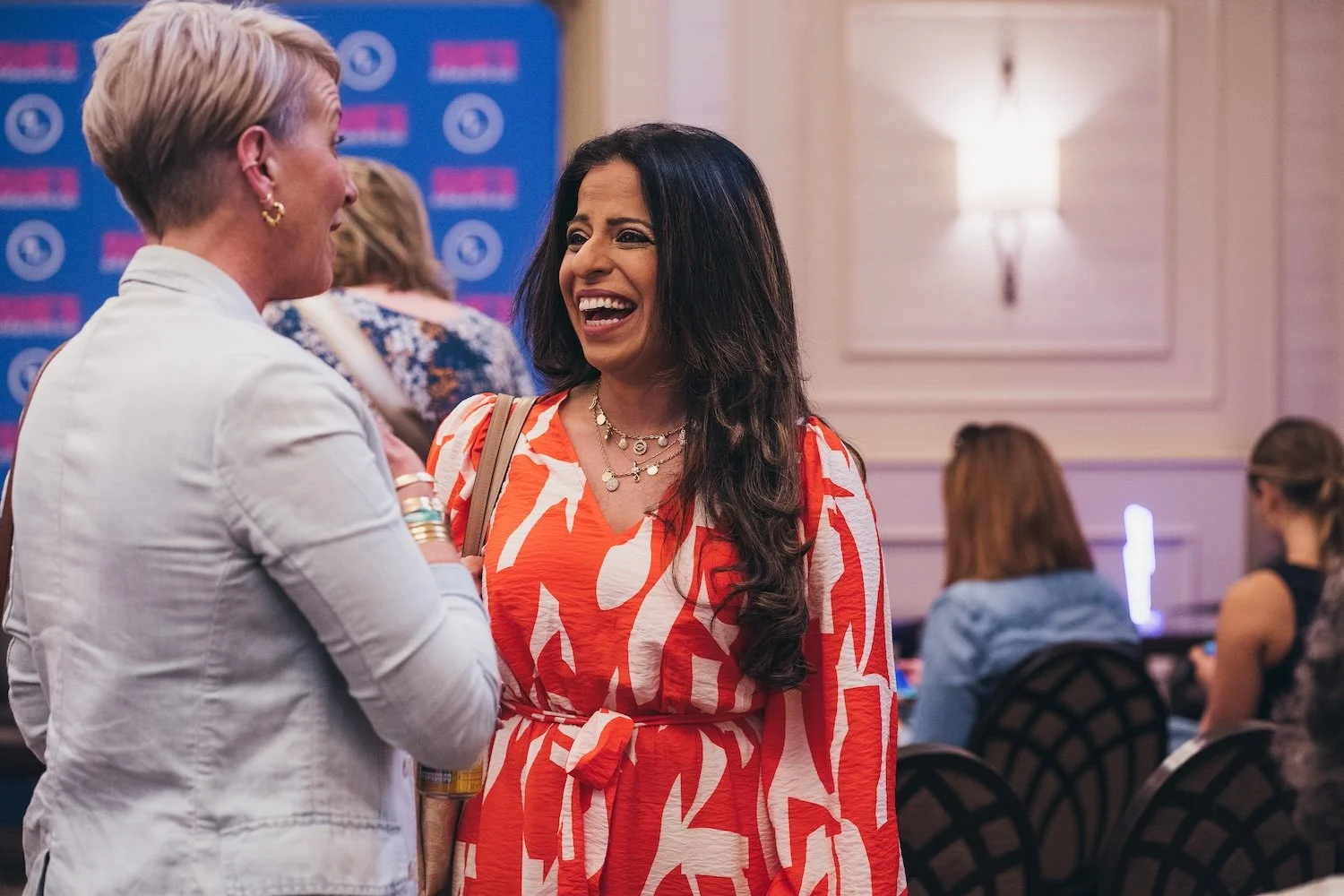 Two women having a conversationat a She's Electric event, with others seated in the background.