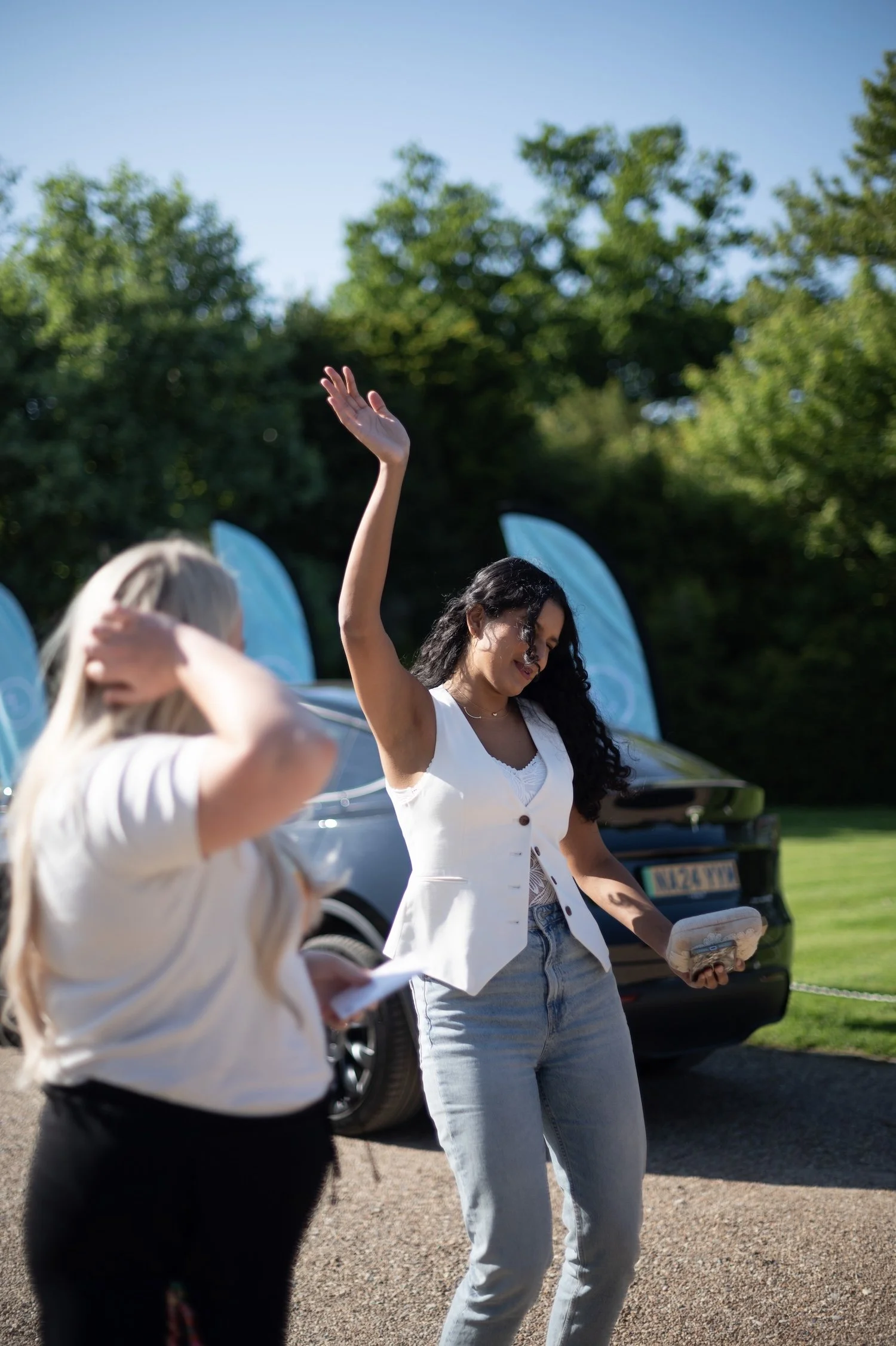 Women dancing outdoors near a Telsa in the background on a sunny day at a She's Electric event