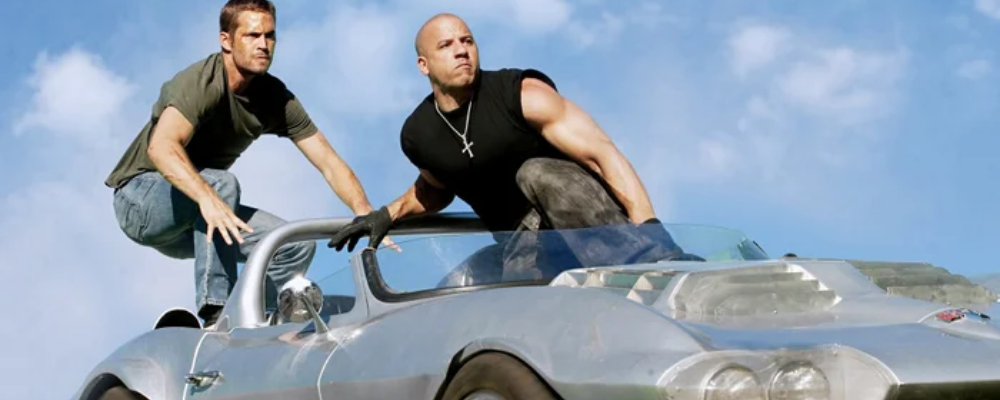 Still from the Fast & Furious film series showing Vin Diesel and Paul Walker standing on top of a car