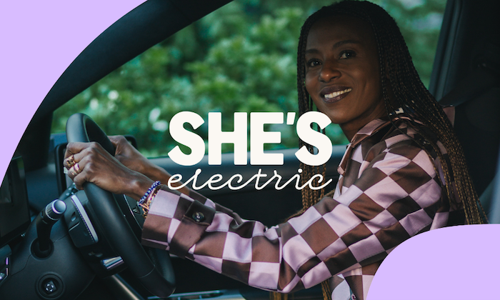She's Electric logo overlaid on a woman doing a test drive at an event