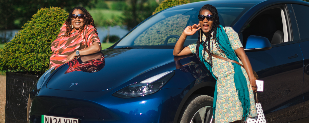Women posing by a blue Tesla at a She's Electric event.