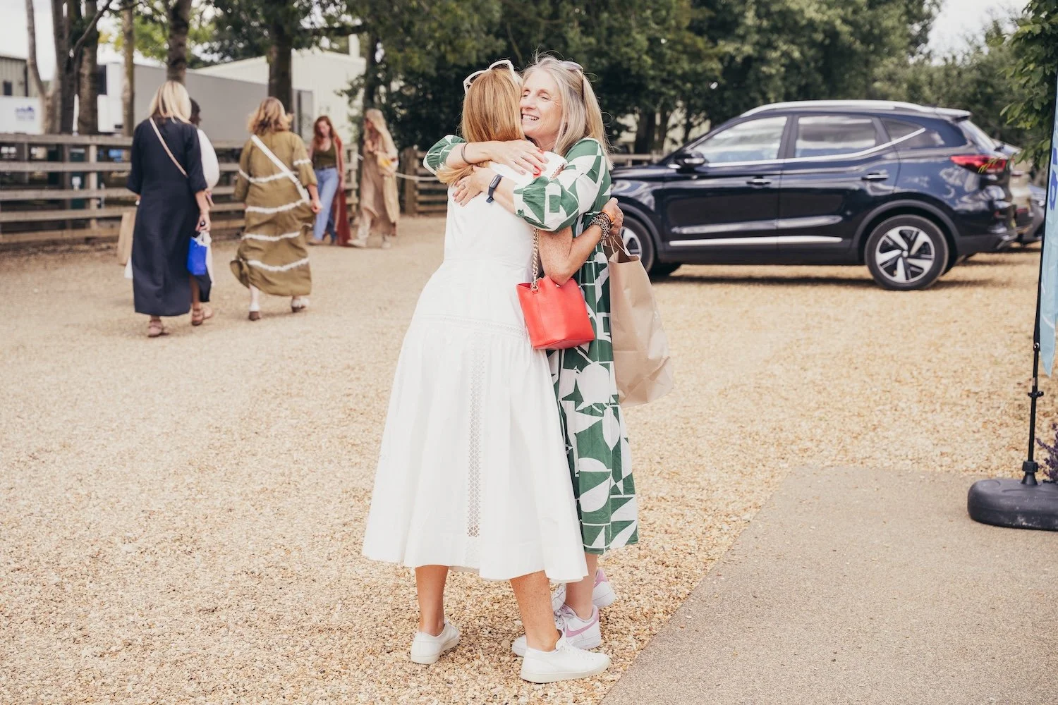 Two women embrace and hug each other while smiling, outdoors at a She's Electric event with Volvo
