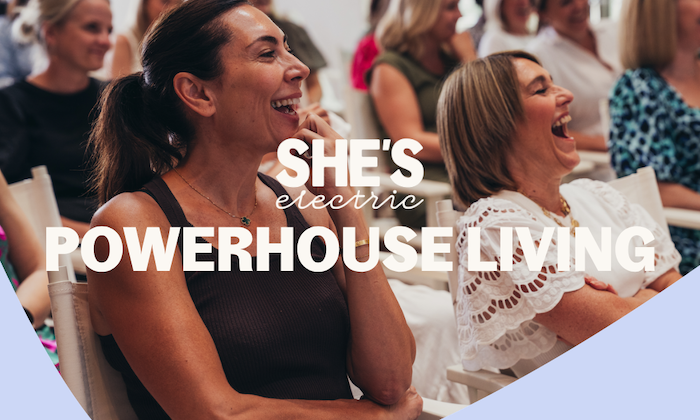 She's Electric Power House Living logo overlaid on an audience of women laughing at an event